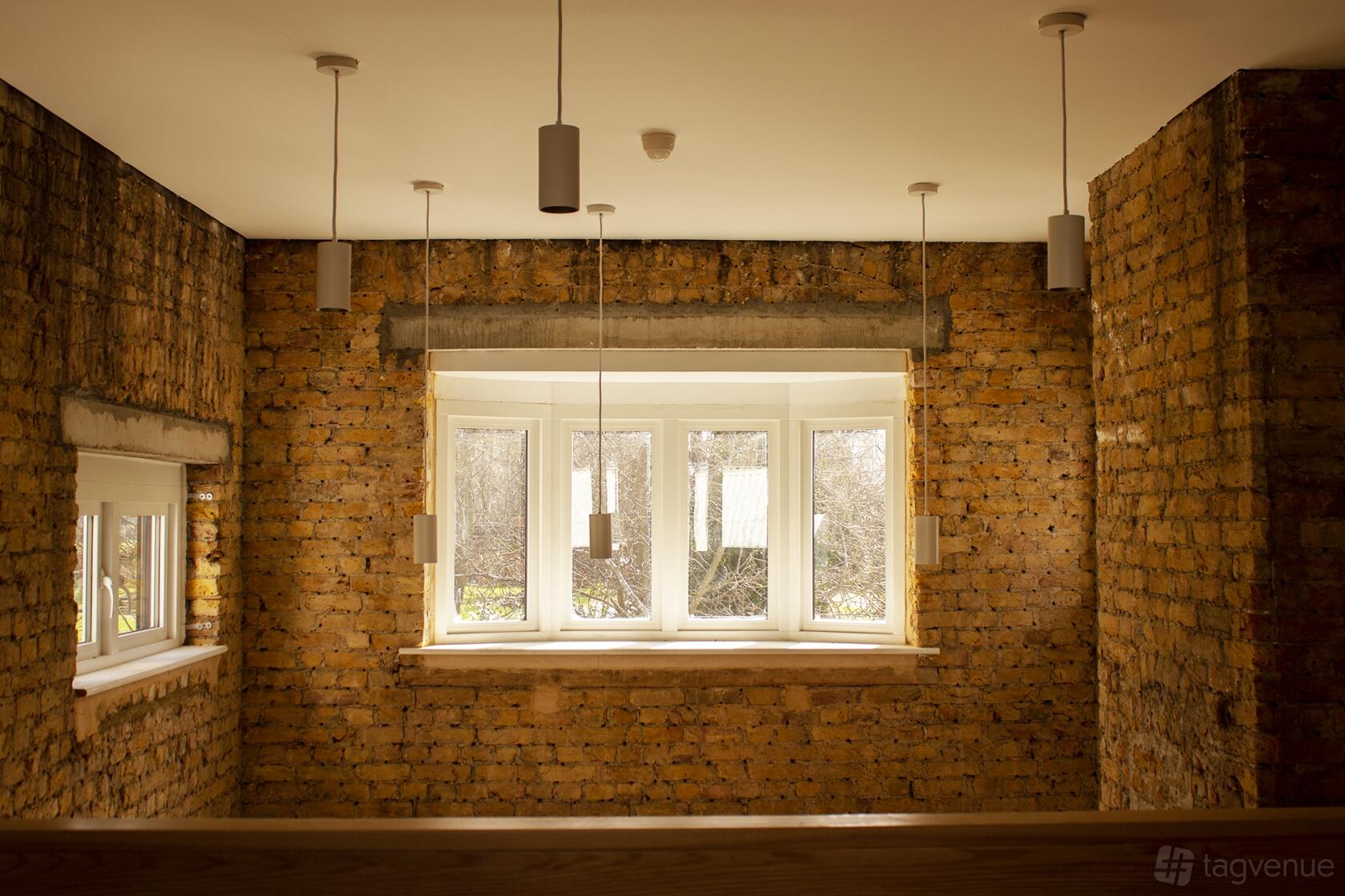 A meeting room with exposed brick walls, pendant lighting, and large windows at Sands End Arts & Community Centre.