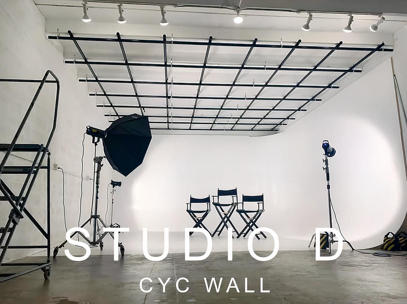 A photo studio with a seamless white cyc wall, overhead grid, director chairs, and photography lights at Wuul Studios - Studio D.
