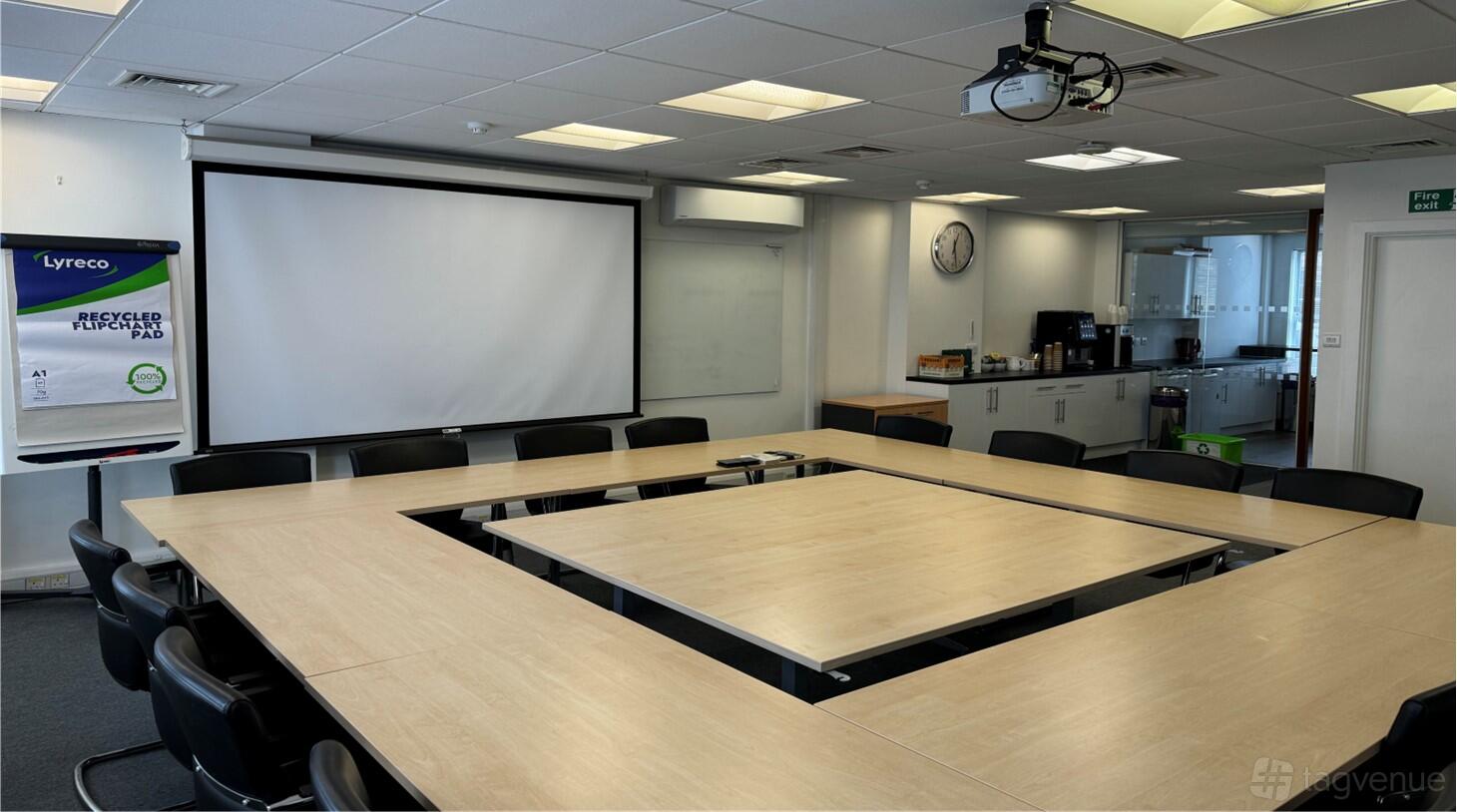 A meeting room with a U-shaped conference table setup, projector, large screen, and whiteboard at FMB Meeting Rooms.