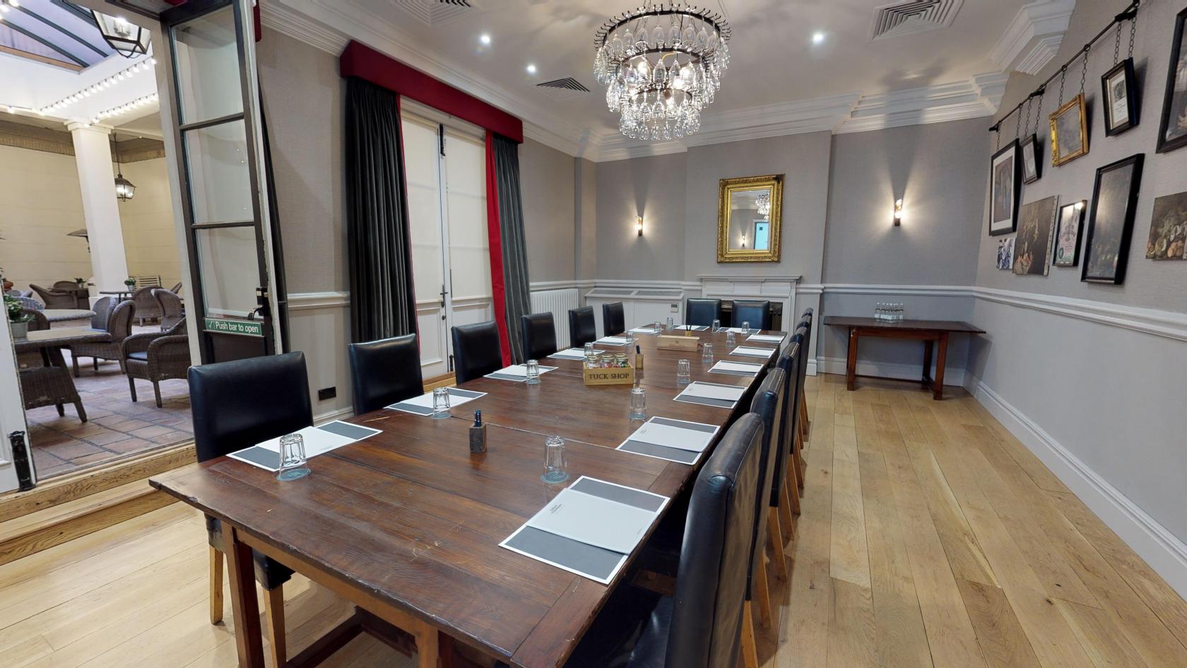 A meeting room with a long wooden table, black leather chairs, chandeliers, and natural light at Hotel du Vin Birmingham.