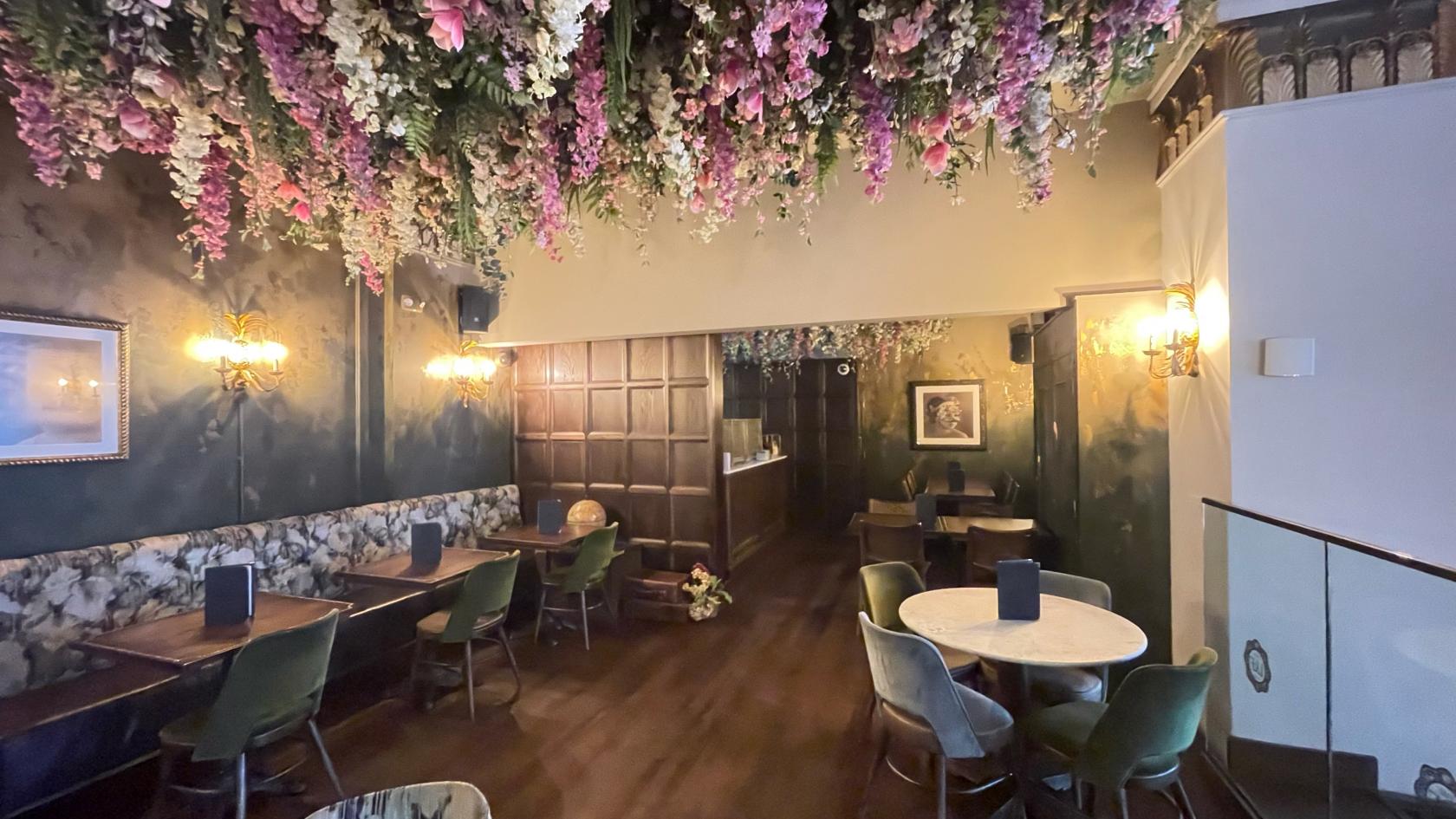 An event space in a restaurant with floral ceiling installations, patterned banquette seating, and wall sconces at The Lost & Found Birmingham.