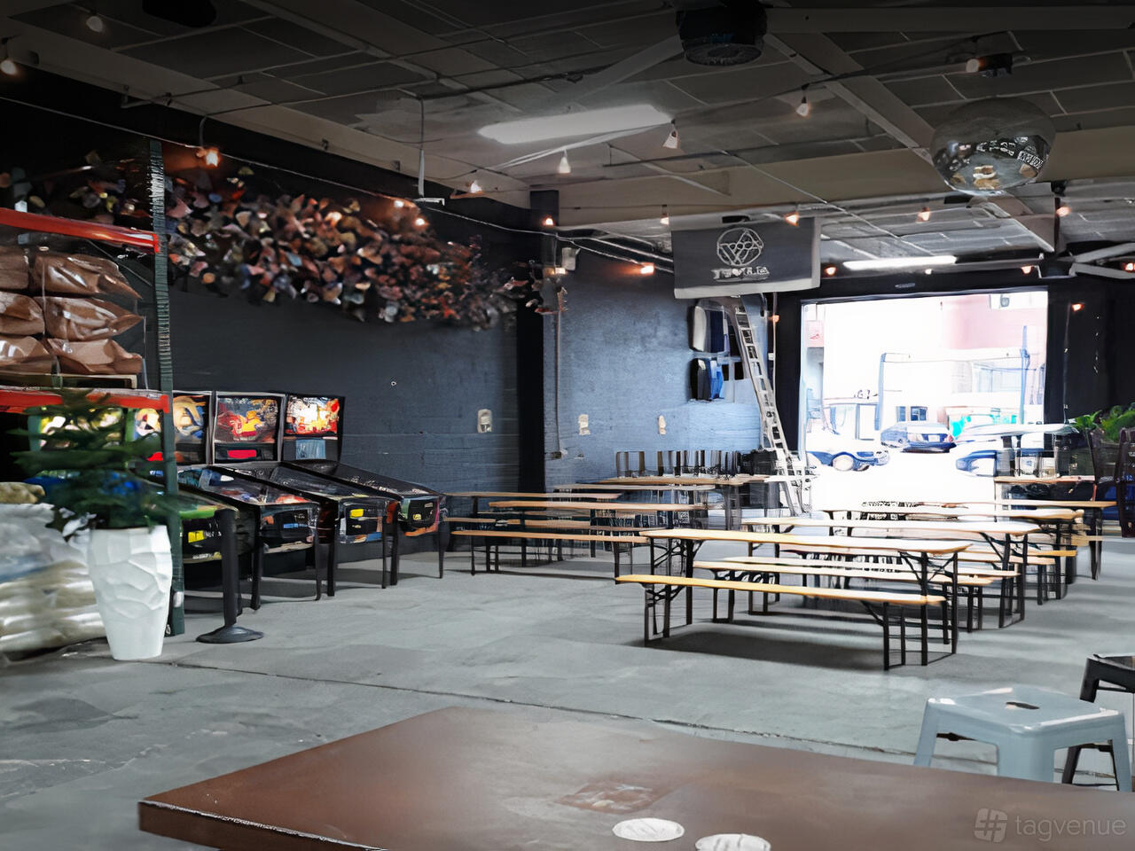 A taproom with long wooden tables, bench seating, pinball machines, and exposed ceiling at Alewife Brewing.