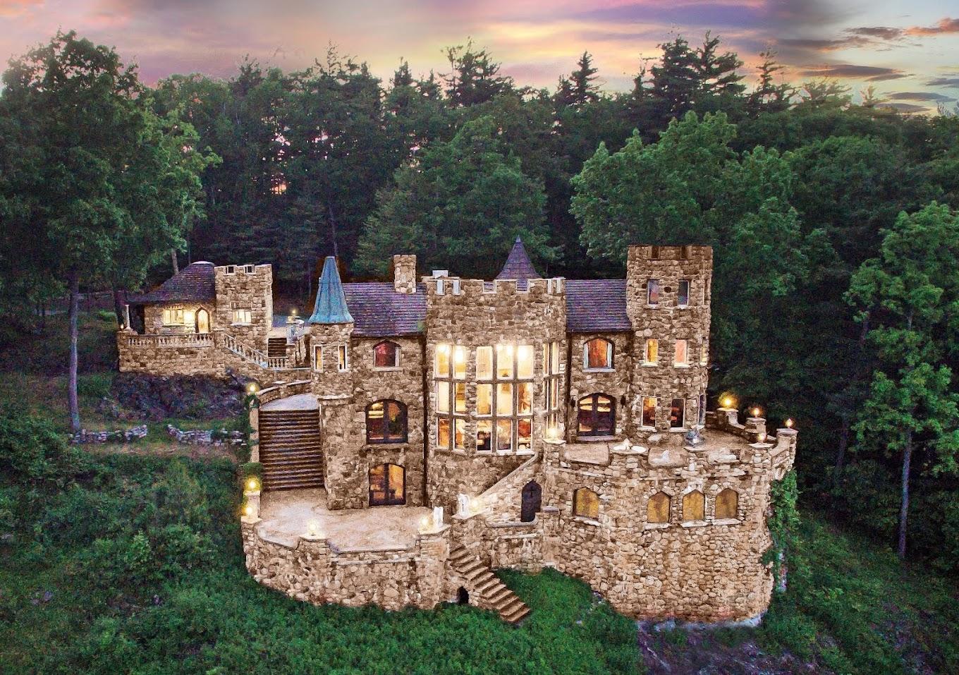 A stone castle with illuminated windows, turrets, and a large terrace surrounded by trees at Highlands Castle.