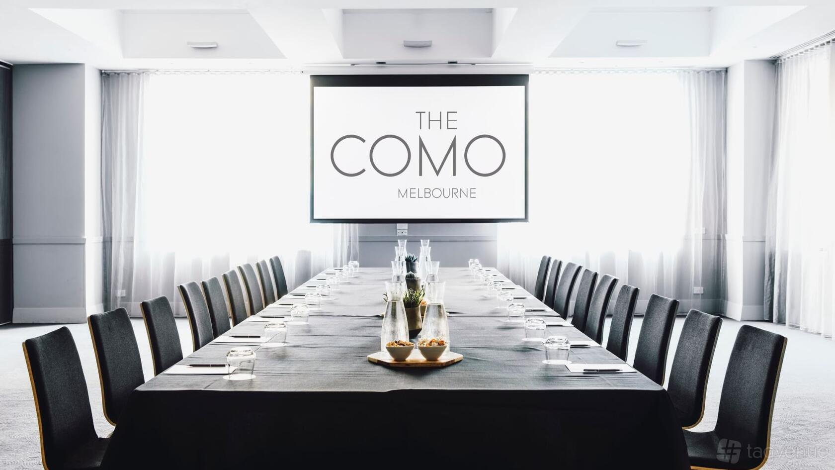 A meeting room with a long conference table, black chairs, and a large projection screen at The Como Melbourne.