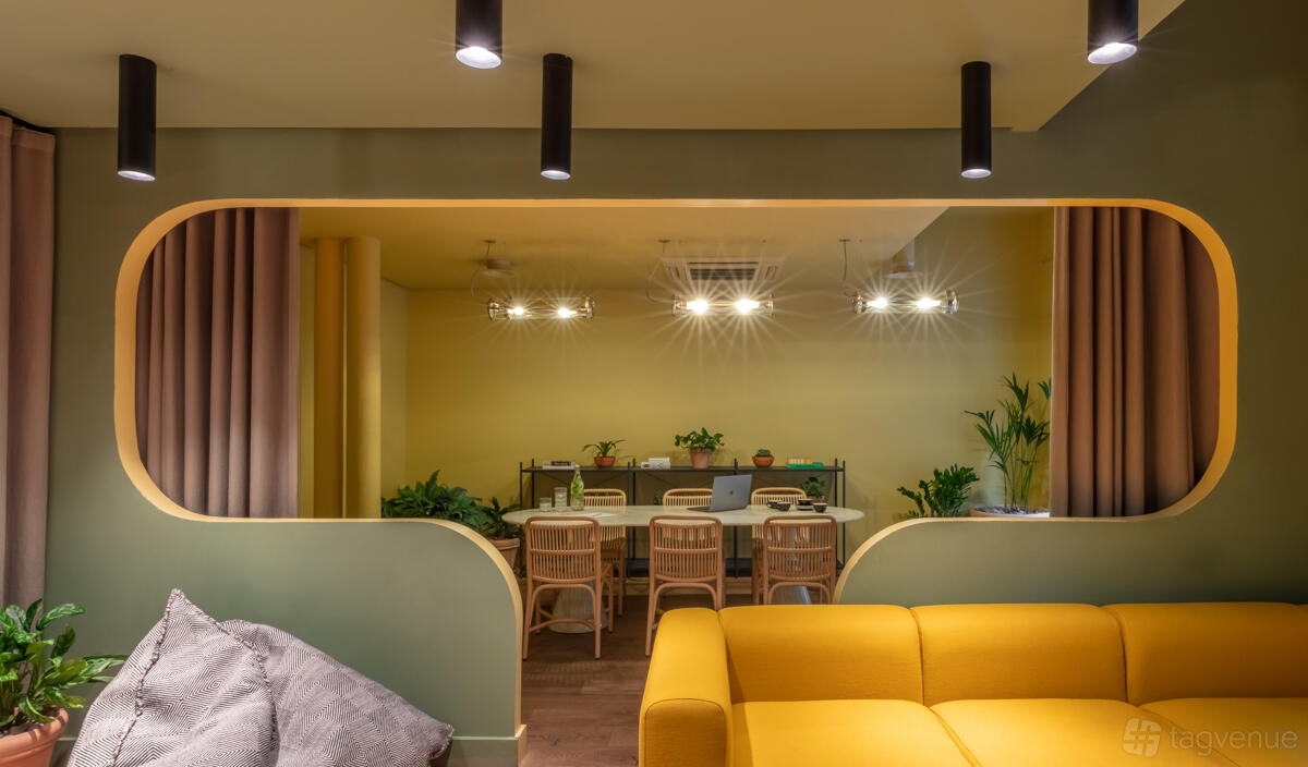 A hotel meeting room with a yellow sofa, large interior window, and a table with wooden chairs at Whitworth Locke Hotel Manchester.