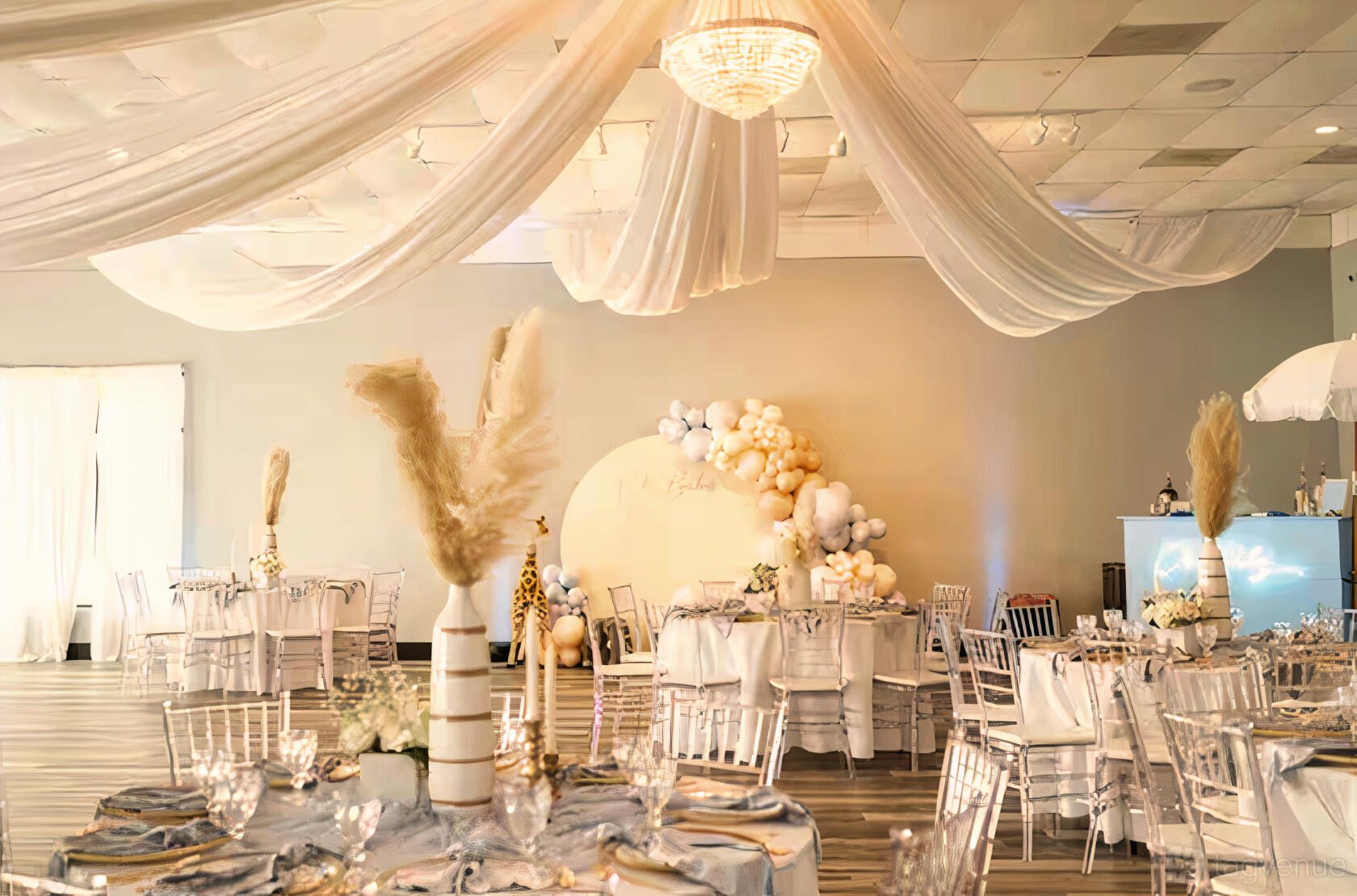 An event venue with draped white fabric ceiling, round tables with silver chairs, and a balloon backdrop at Memories Event Space.