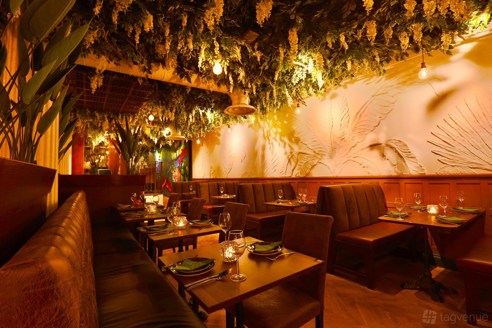 An event space in a restaurant with hanging greenery, carved botanical wall art, and intimate table seating at PARO.