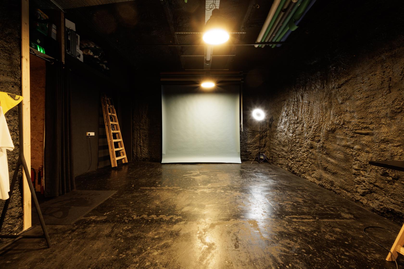 A film studio in a loft with textured dark walls, overhead lighting, and a photography backdrop at Loft Style Studio Hire.