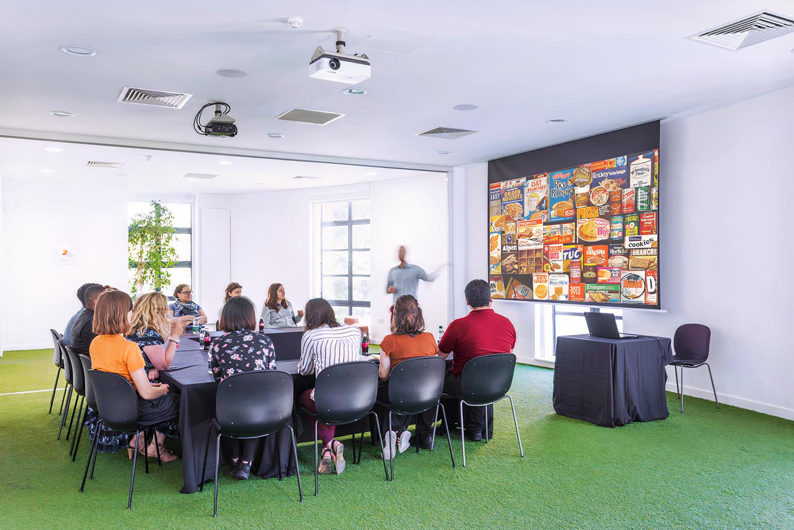 A conference room with green carpet, large windows, and a projector screen at Museum of Brands.