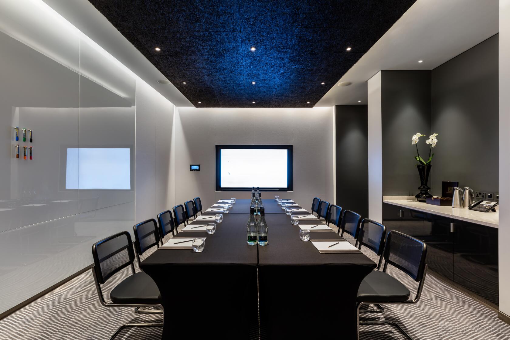 A hotel meeting room with a long conference table, black chairs, large screen, and a refreshment station at Radisson Blu Hotel, London Mercer Street.