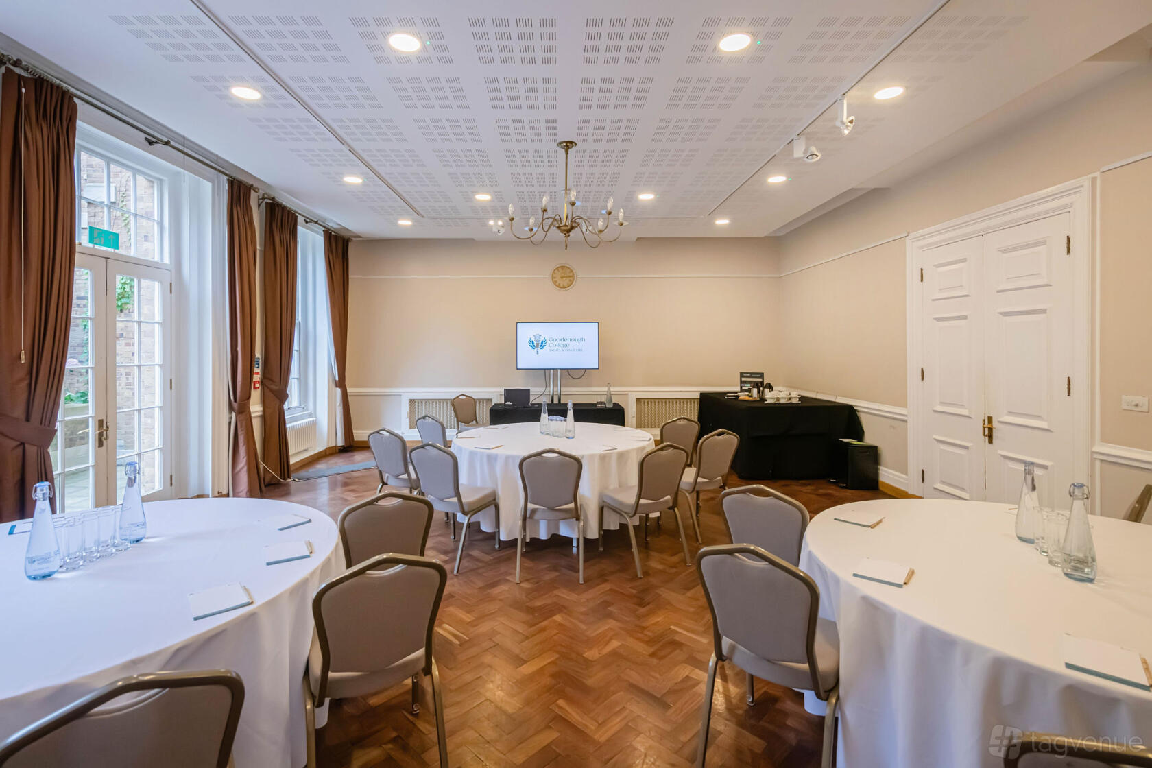 A meeting room with round tables draped in white linens, parquet flooring, and large windows at Goodenough House.