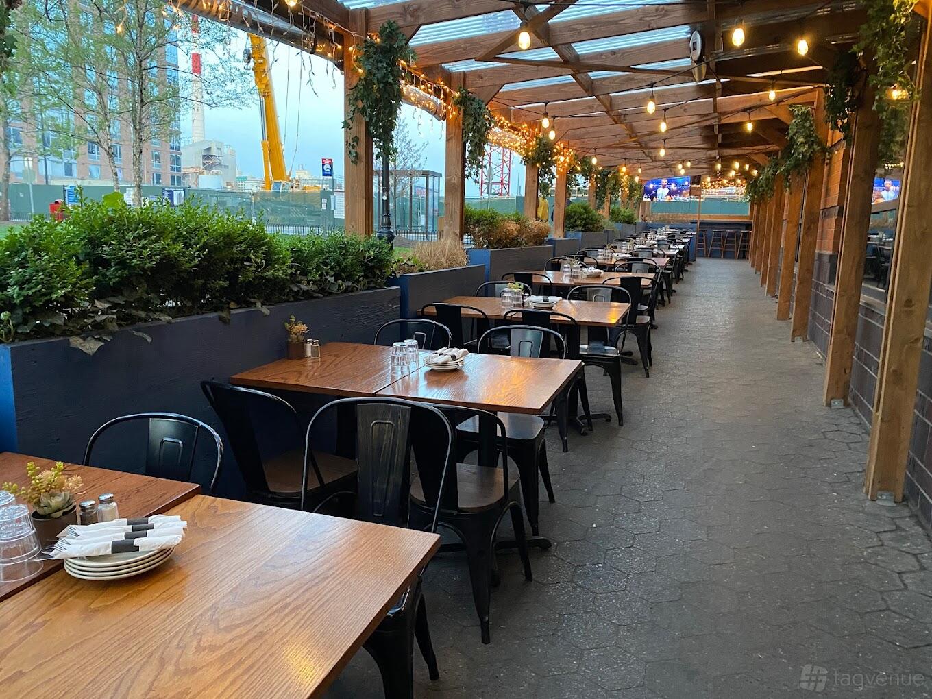 A covered terrace with wooden tables, black chairs, hanging string lights, and greenery at Granny Annie's Bar & Kitchen.