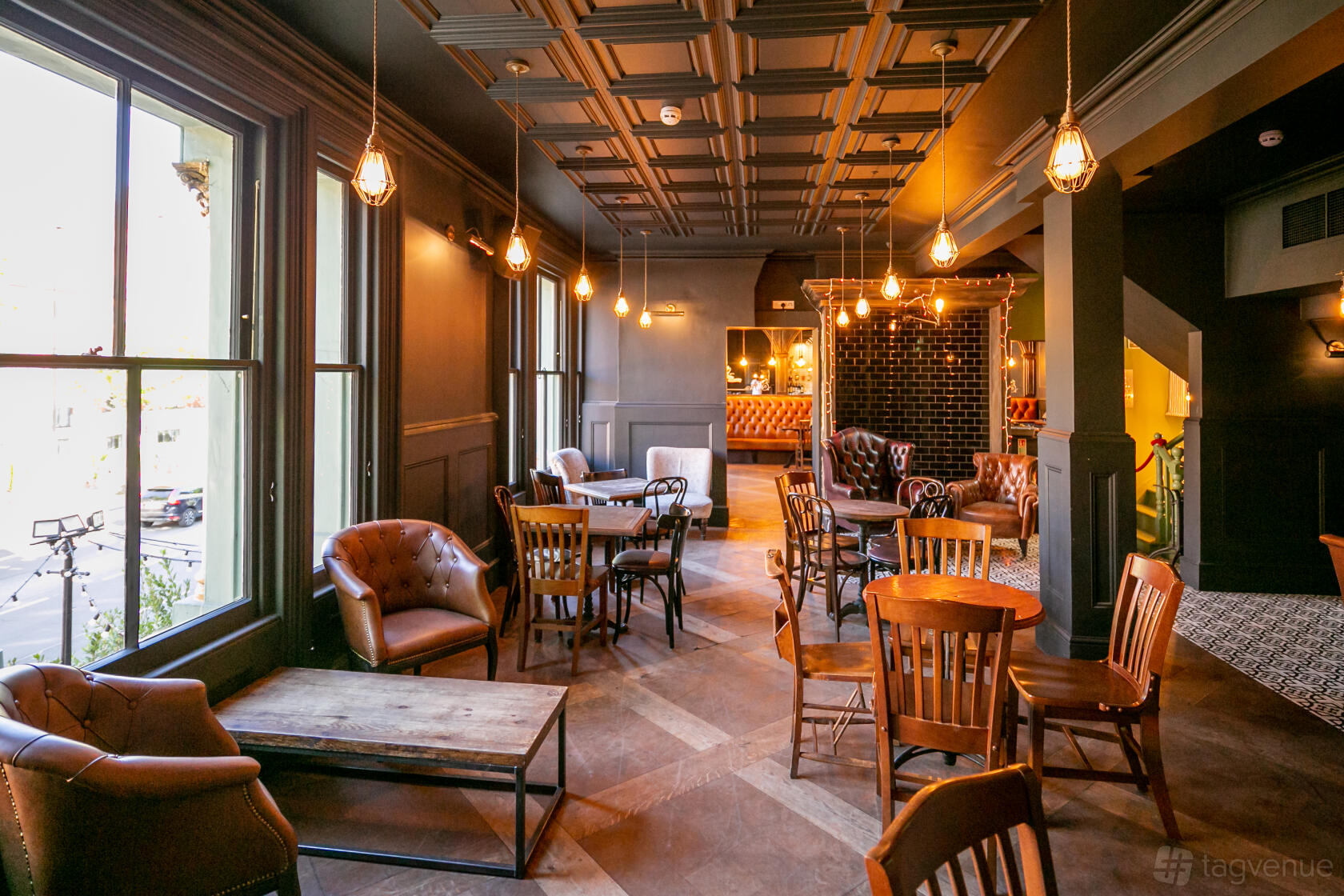 A function room in a pub with vintage leather armchairs, wooden tables, and hanging pendant lights at Owl & Hitchhiker.