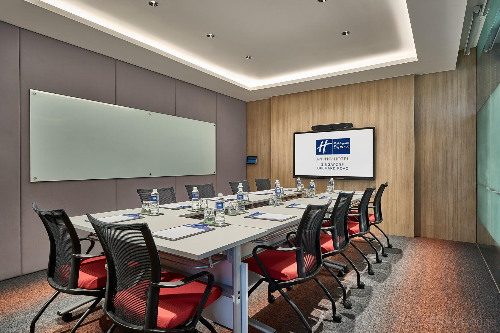 A meeting room with a long conference table, ergonomic chairs, wall-mounted screen, and glass whiteboard at Holiday Inn Express Singapore Orchard Road.
