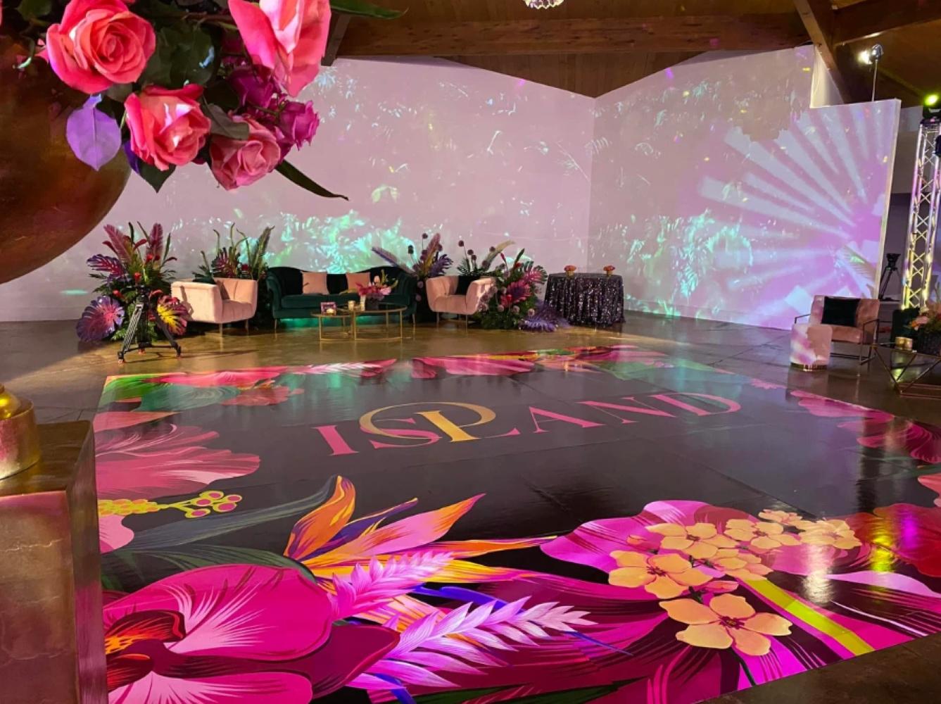 A hall with a floral-themed dance floor, lounge seating, and decorative pink flower arrangements at The West Venue.