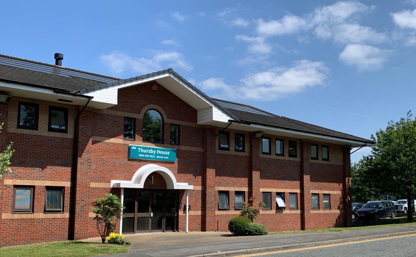 A coworking space with a red brick exterior, arched windows, and landscaped shrubs at UBC Thursby House.