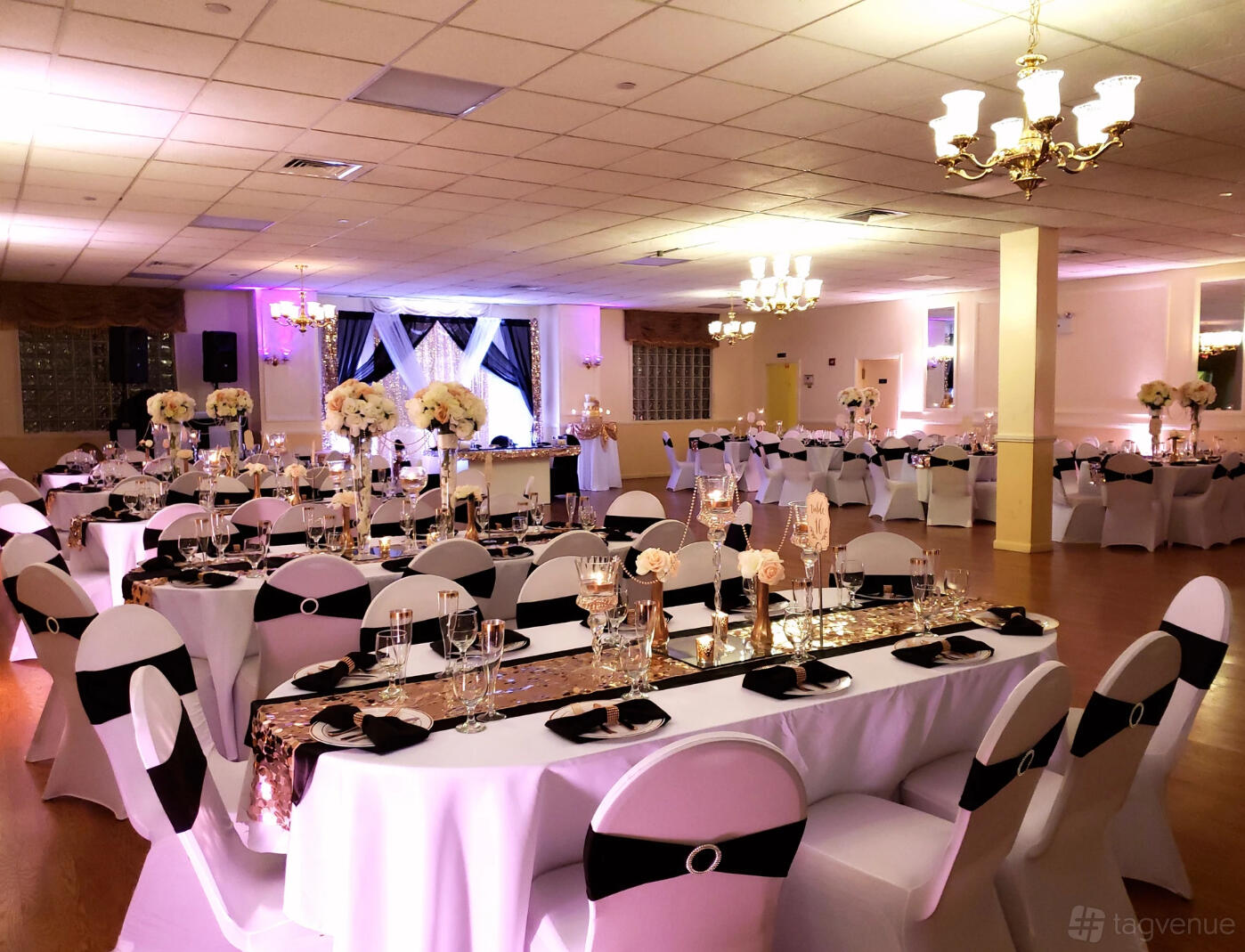 A banquet hall with long rectangular tables, white chair covers, gold sequin runners, and floral centerpieces at Occasions Banquet & Catering Hall.