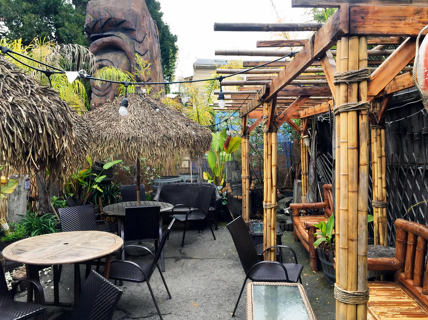 An outdoor patio with bamboo pergolas, thatched umbrellas, and wicker chairs at Forbidden Island Tiki Lounge.