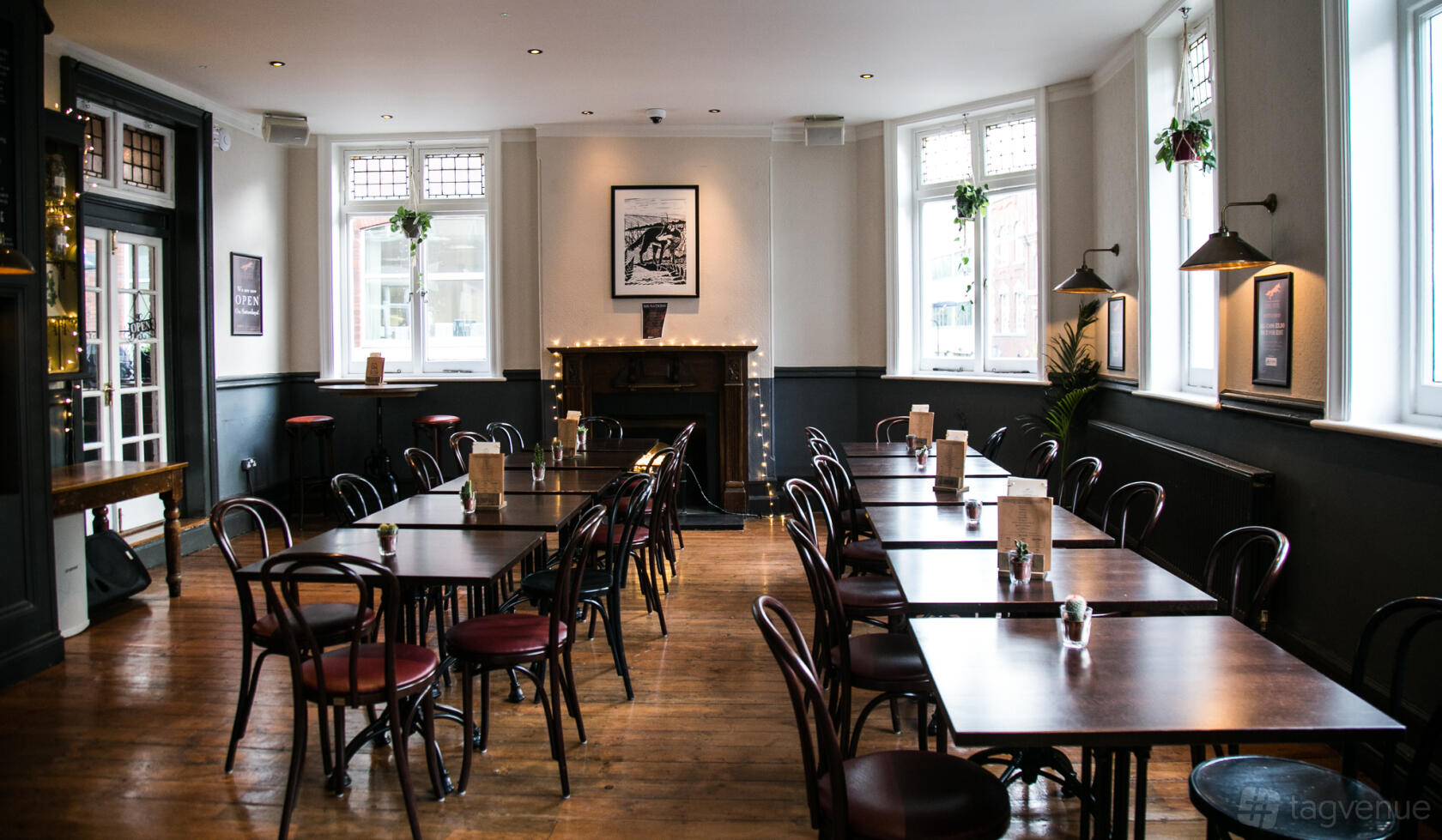 A pub with wooden floors, dark chairs, large windows, and a decorative fireplace at The Fox, Shoreditch.