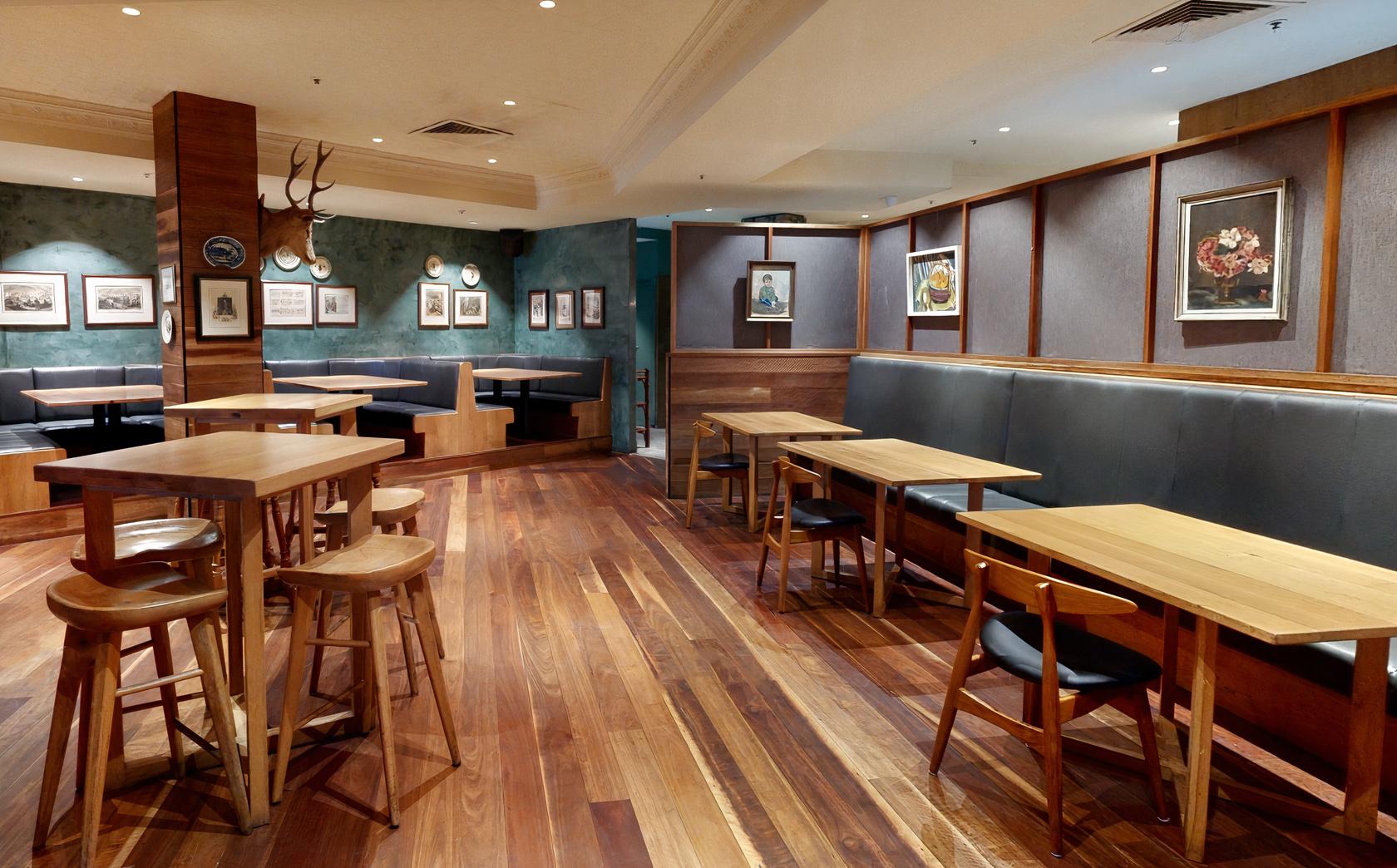 A dining room with wooden floors, framed artwork on muted teal walls, and simple wooden tables at Pig ‘N’ Whistle - Indooroopilly.