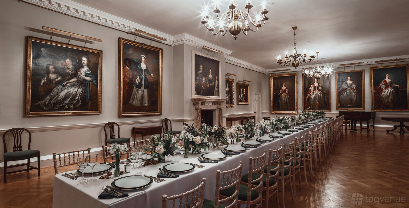 A gallery with classical portraits, chandeliers, and a long banquet table with floral centerpieces at The Foundling Museum.