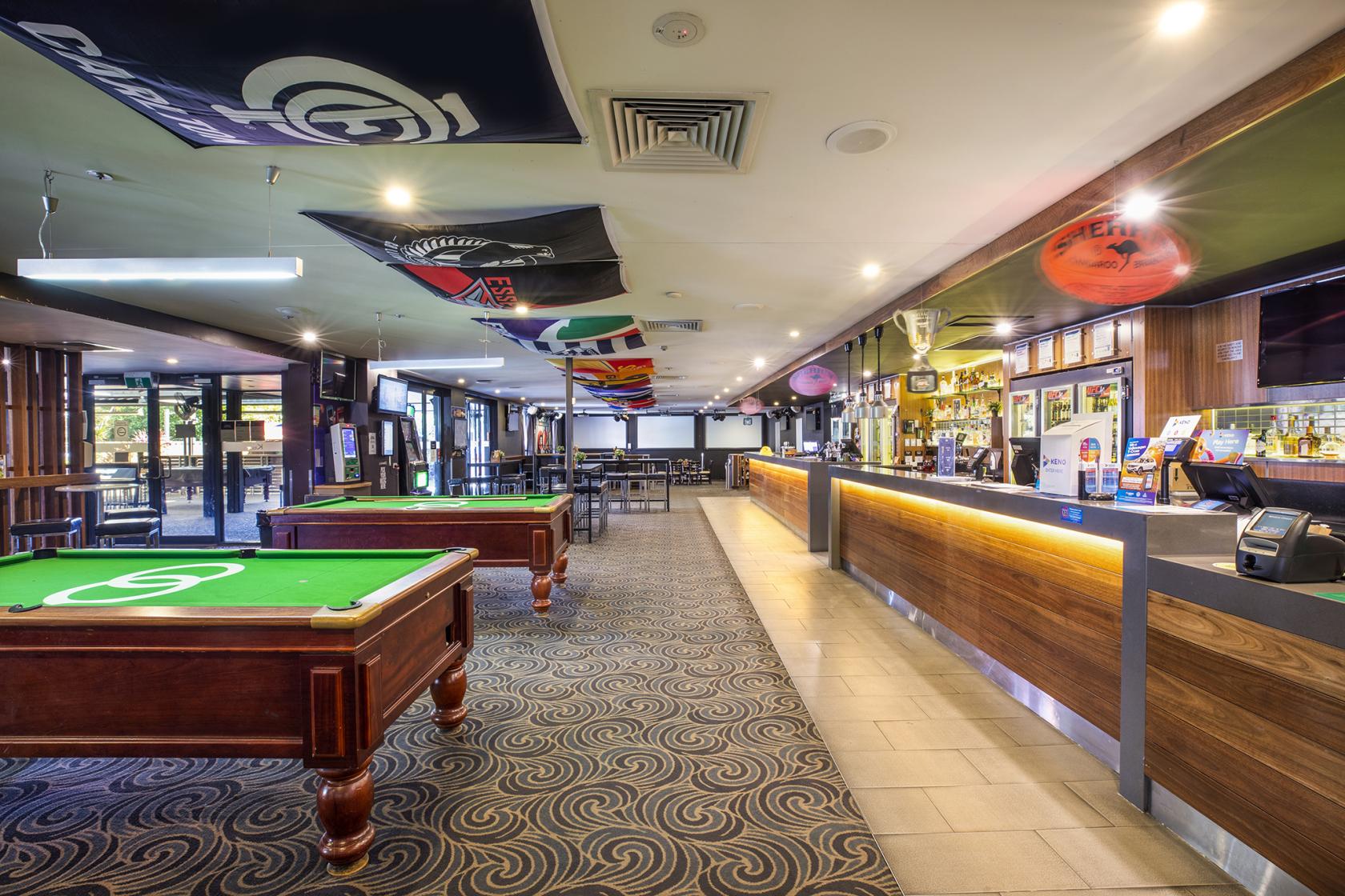 An event space in a pub with pool tables, a long wooden bar, and sports banners at Keysborough Hotel.