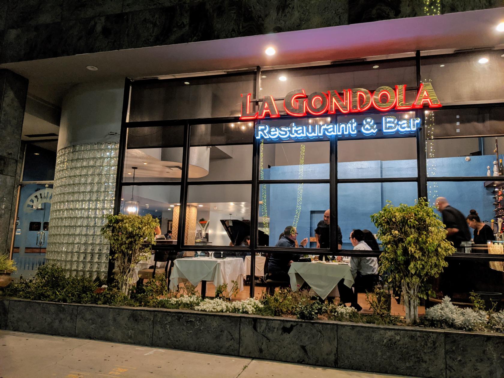 A restaurant with floor-to-ceiling windows, neon signage, and white tablecloths at LA Gondola.
