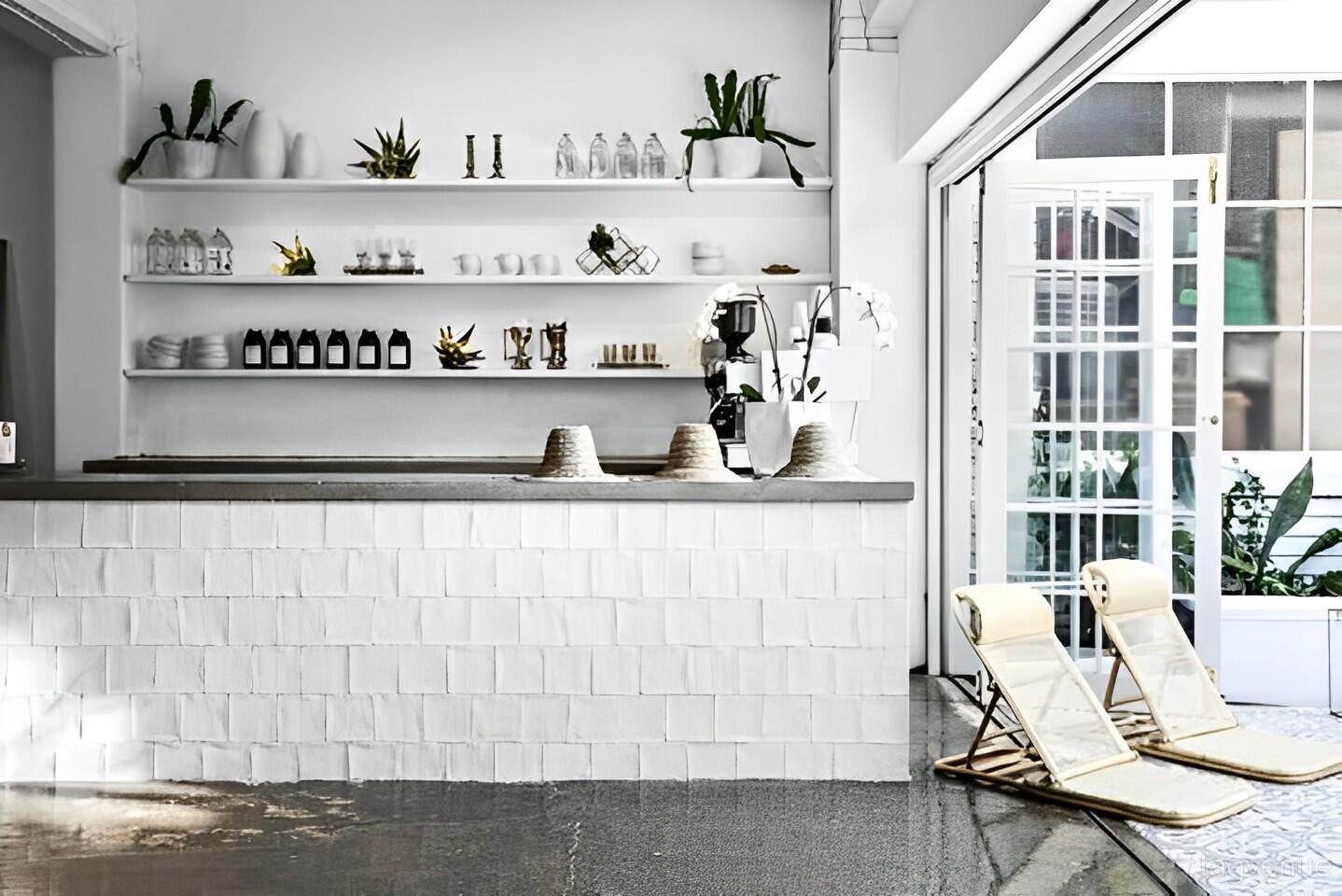 An event venue with a white-tiled bar, open shelving with plants, and lounge chairs by a glass wall at La Porte Space.