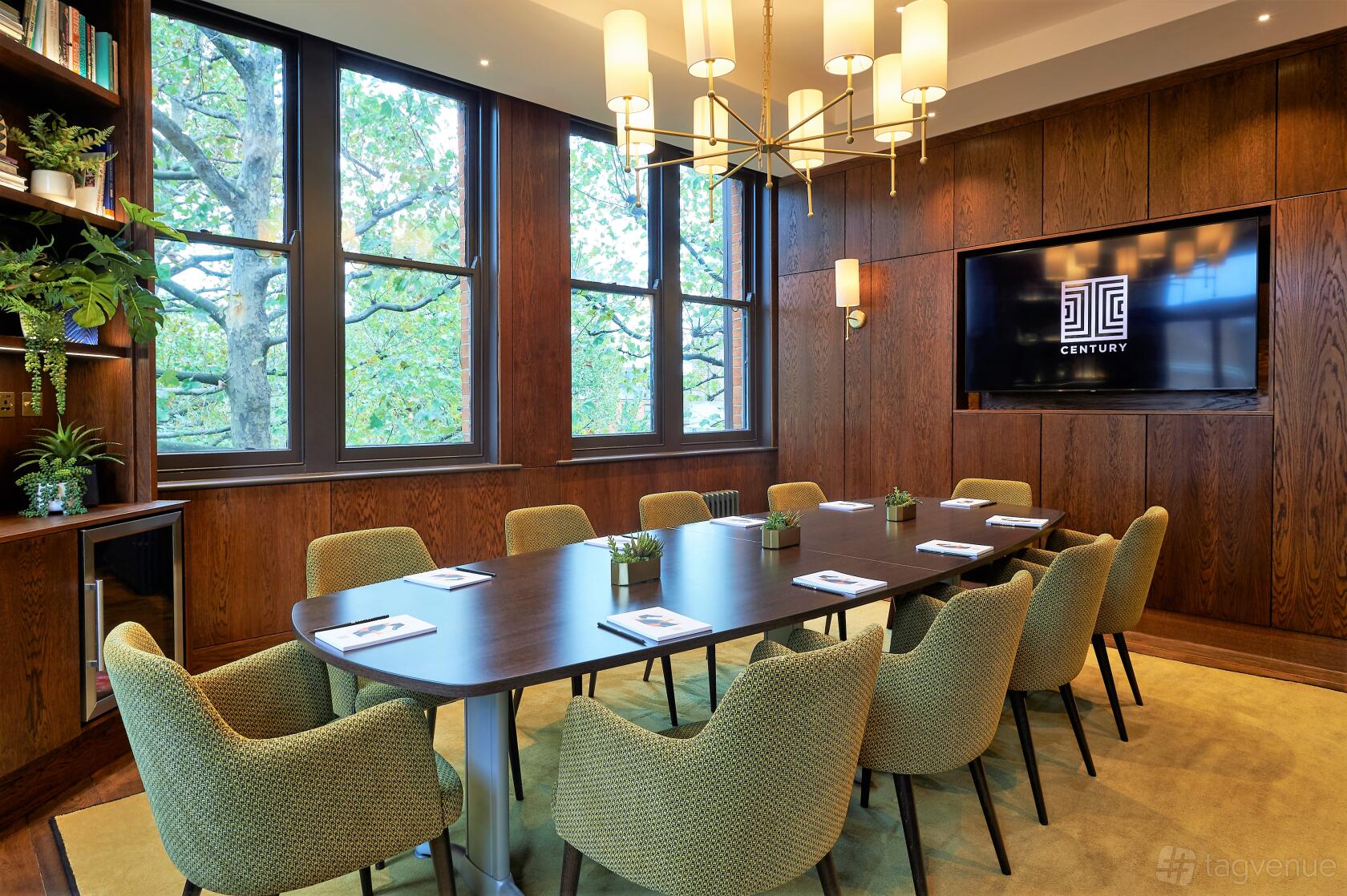 A meeting room bar with a long oval table, green upholstered chairs, wood panel walls, and large windows at Century Club.