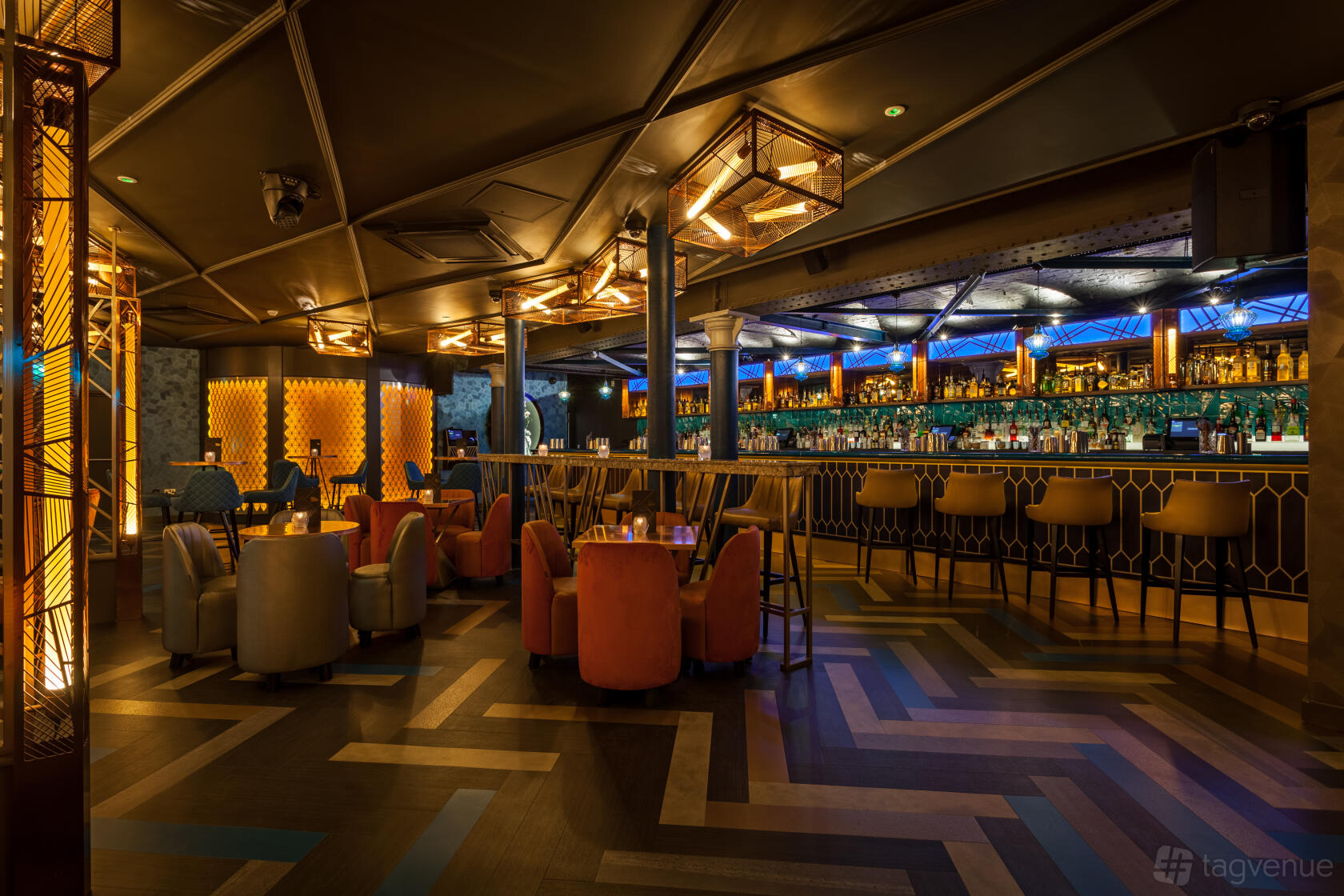 A cocktail bar with geometric flooring, ambient lighting, and a long illuminated bar at Dirty Martini Manchester.