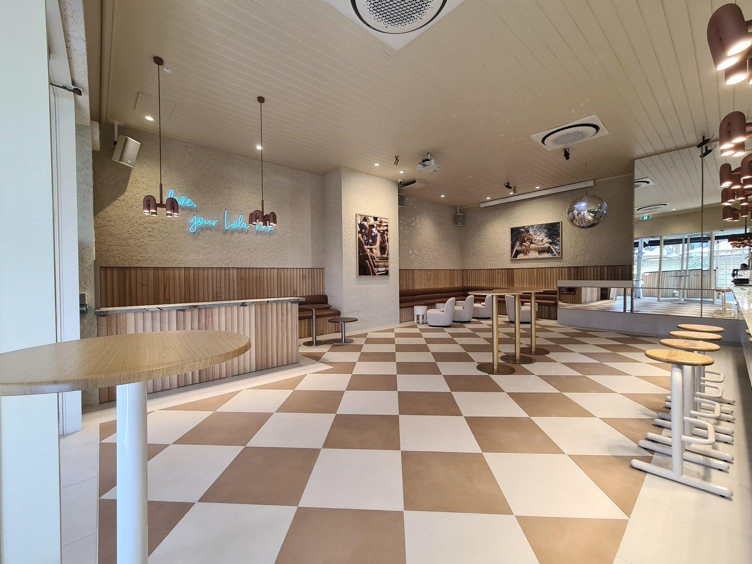 An event venue with checkered floors, round wooden tables, and light wood accents at LOLA St Kilda.