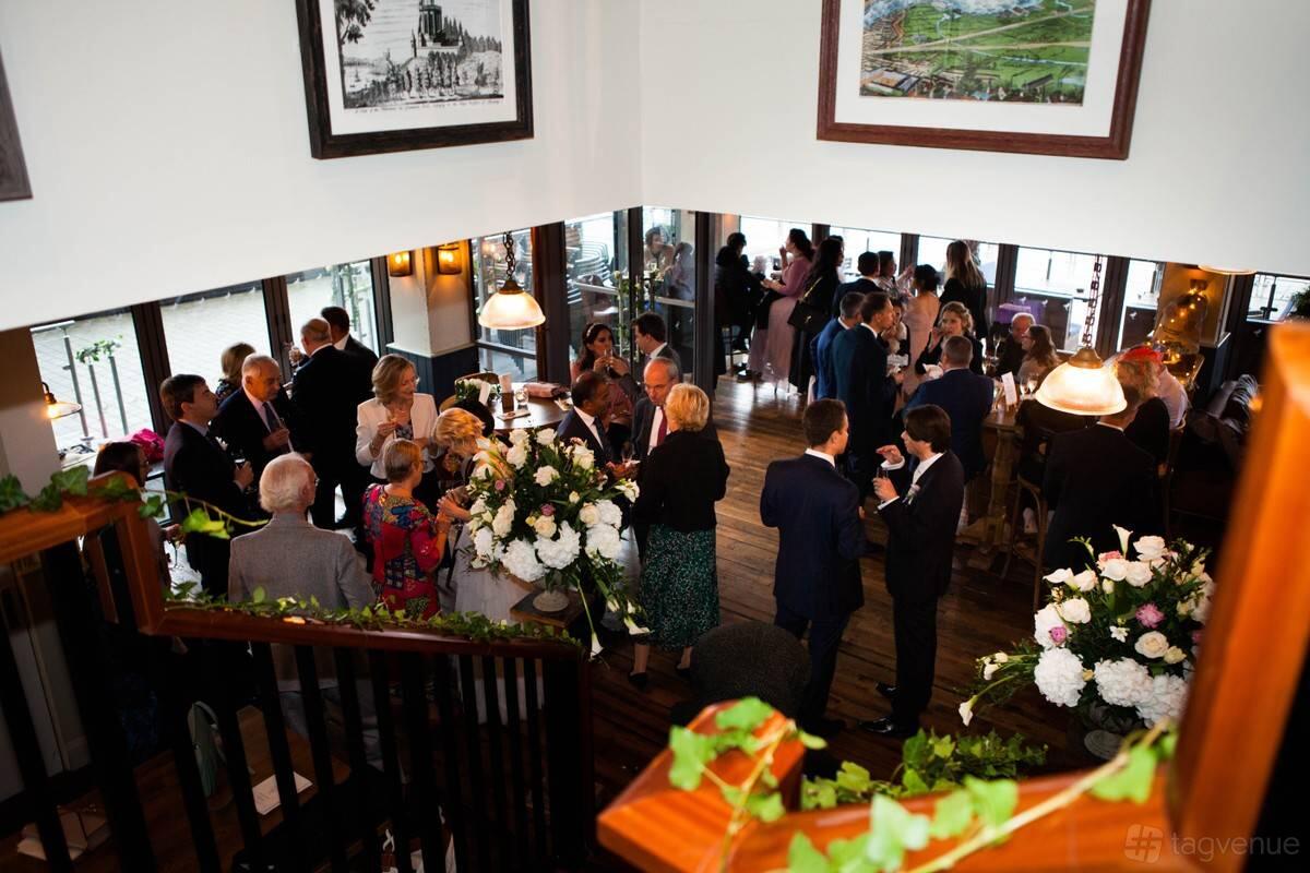 A pub bar with wooden floors, floral arrangements, and framed art on white walls at The Oystercatcher.
