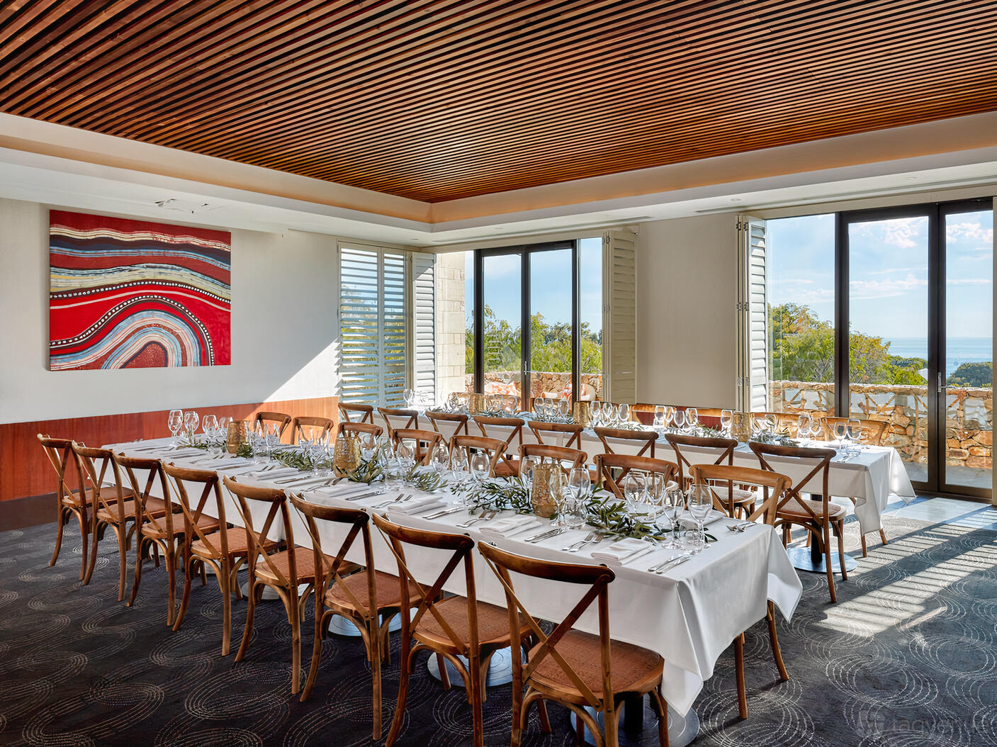 A hotel meeting room with floor-to-ceiling windows, two long banquet tables, and wooden chairs at Pullman Bunker Bay.