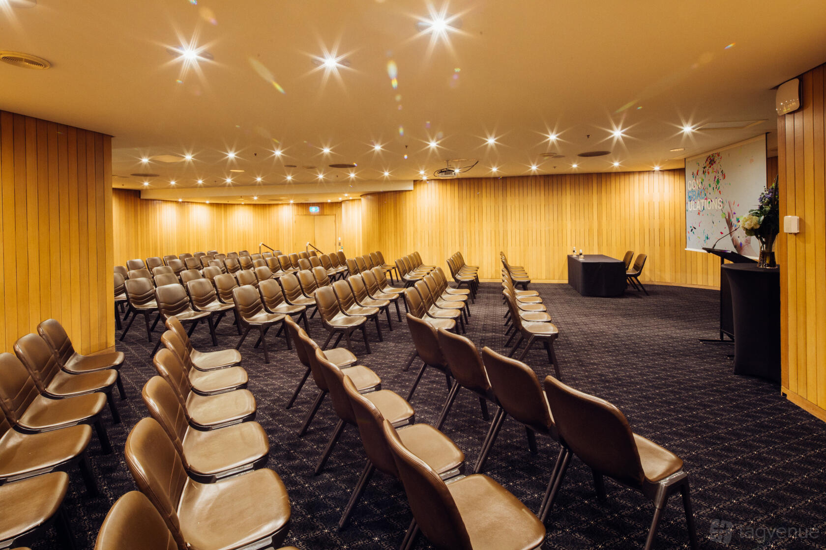 A meeting room with tiered rows of brown chairs, wood-paneled walls, and ceiling spotlights at Sydney Masonic Centre.