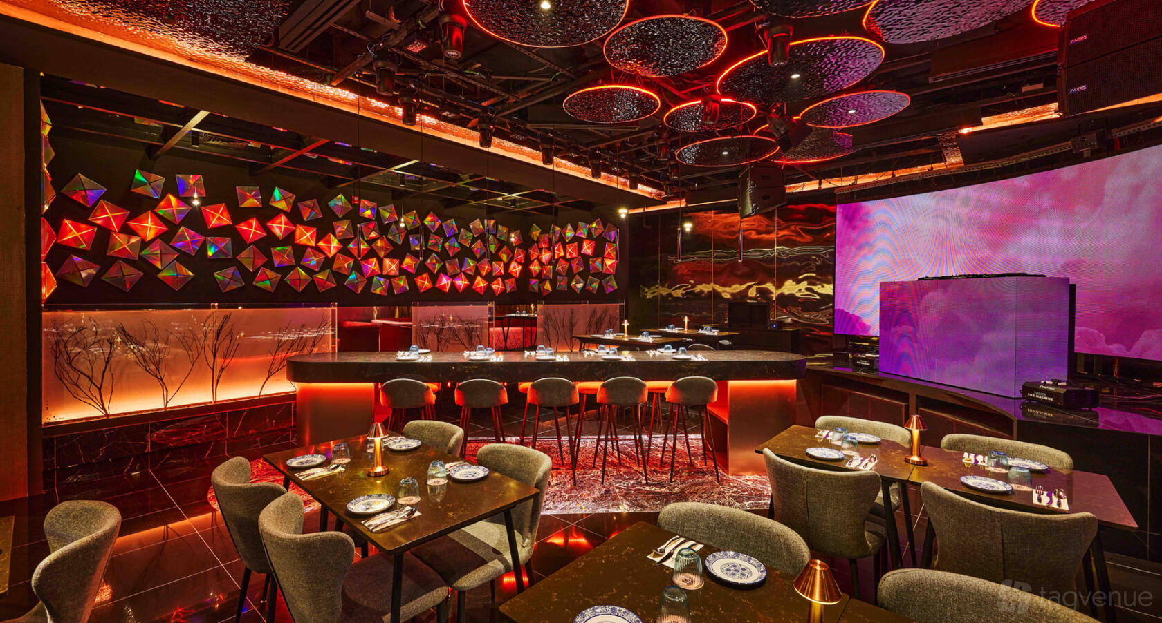 A restaurant interior with colorful geometric wall art, glowing red lighting, and tables set with patterned plates at Synthesis 食拿酒稳.