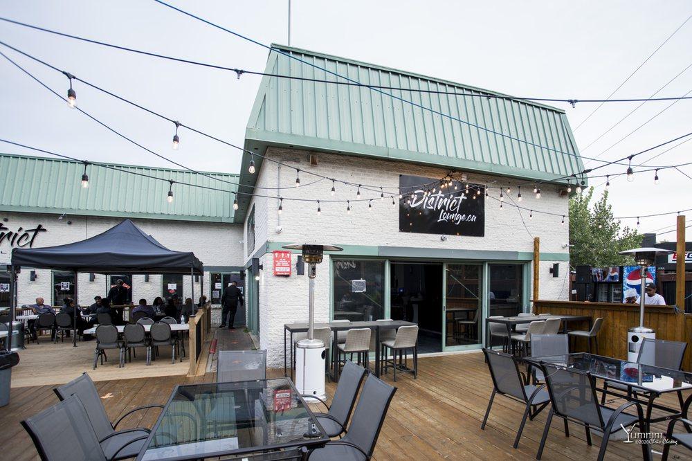 An outdoor nightclub patio with string lights, wooden decking, glass tables, and covered seating at District Lounge.