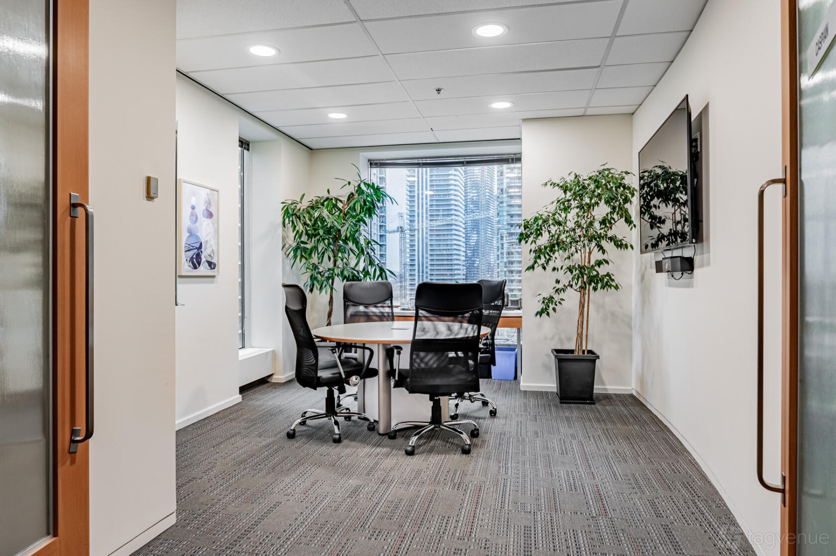 A meeting room with a round table, black chairs, large windows, and potted plants at The Rostie Group.