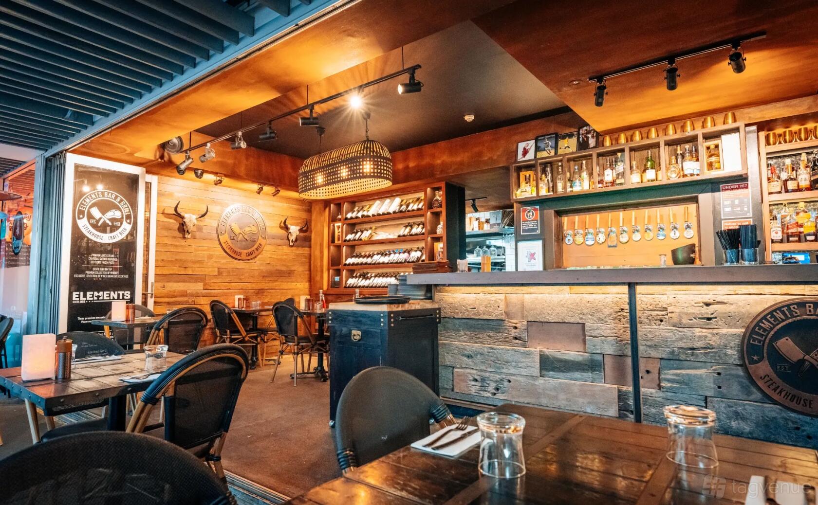 A restaurant with wooden walls, hanging wine racks, and a rustic bar counter at Elements Bar & Grill Darlinghurst.