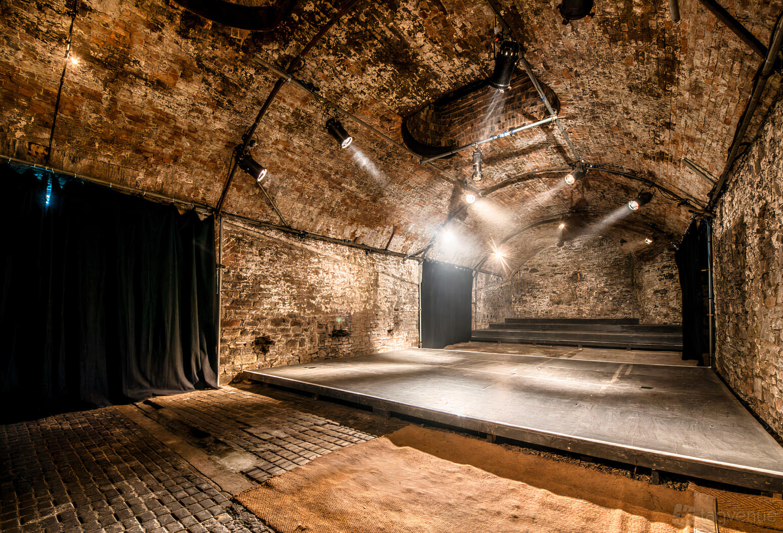 A nightclub with exposed brick vaulted ceilings, stage lighting, and a raised platform at The Loco Klub.
