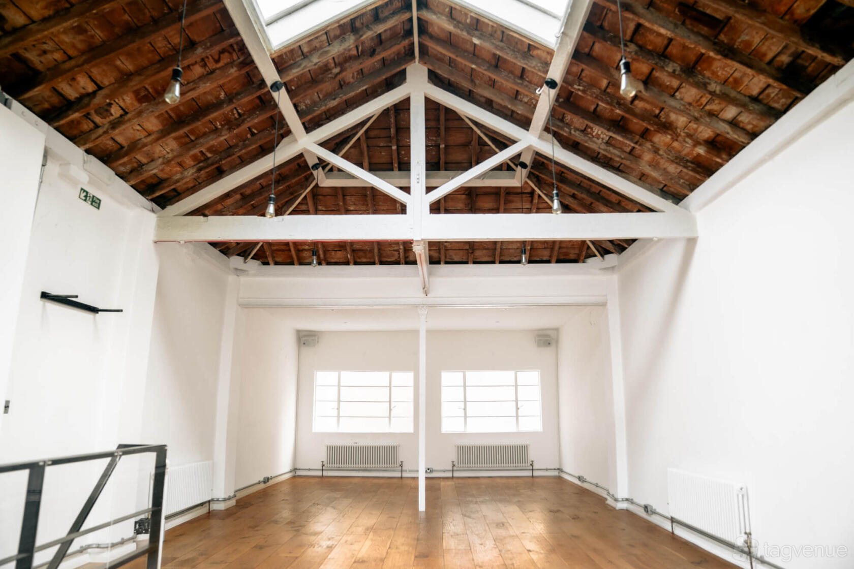 A loft yoga studio with exposed wooden beams, large skylights, and wood floors at Sāmya Studios.