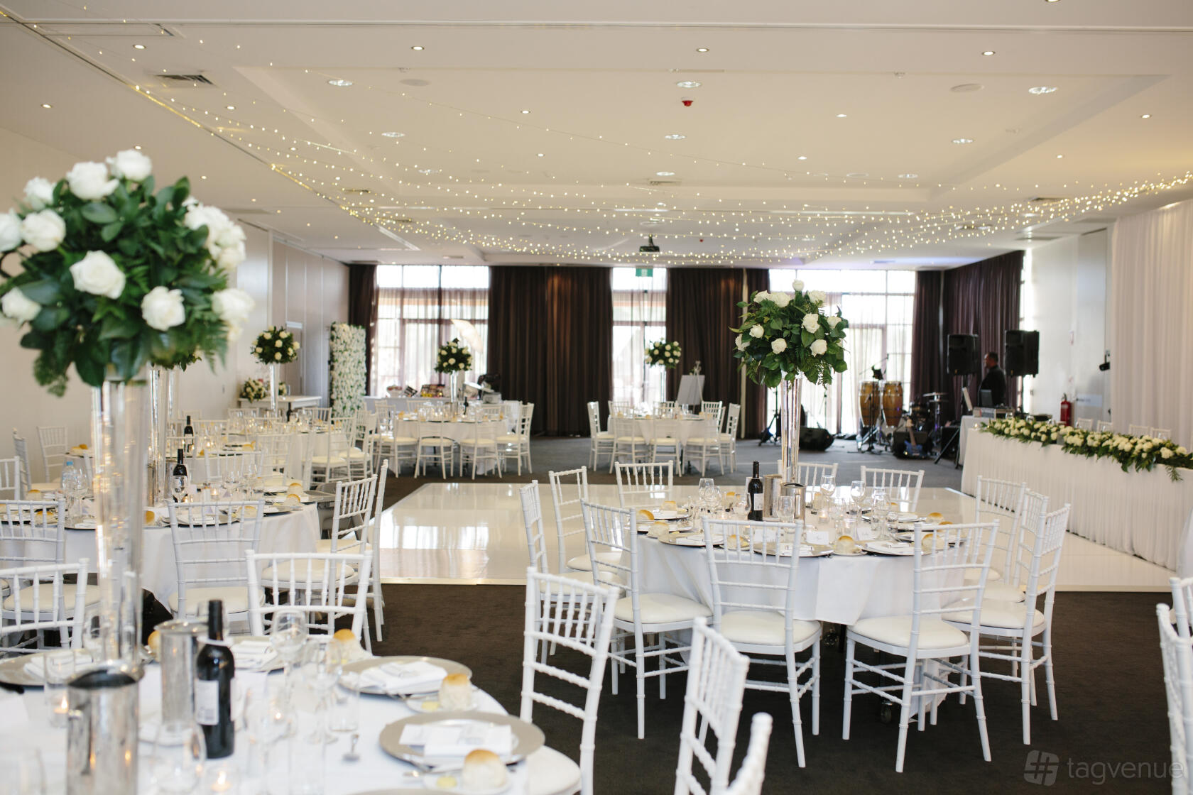 A hotel ballroom with round tables, white chairs, floral centerpieces, and string lights at Mercure Kooindah Waters.