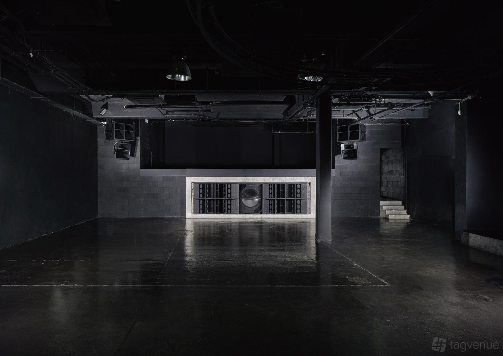 An event venue with dark polished floors, a large speaker wall, and industrial lighting at Studio Spaces.