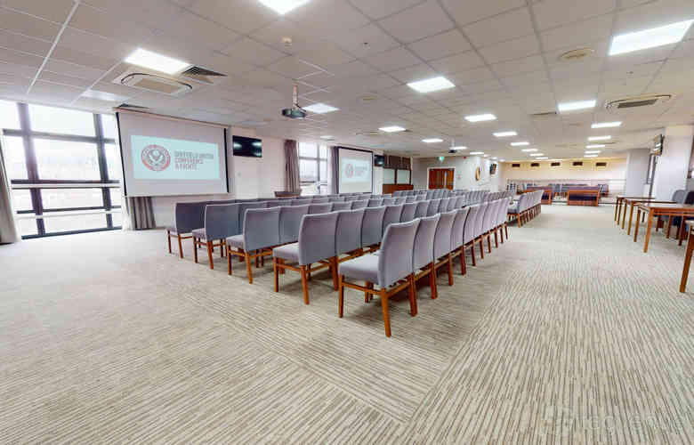 An auditorium with rows of cushioned chairs, projection screens, and floor-to-ceiling windows at Sheffield United Football Club.