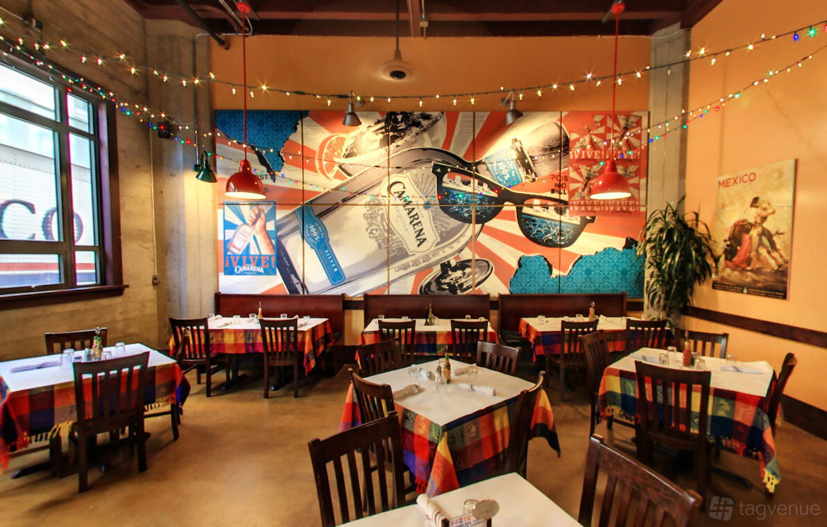 A restaurant with colorful tablecloths, string lights, and a vibrant mural at Cadillac Bar & Grill.
