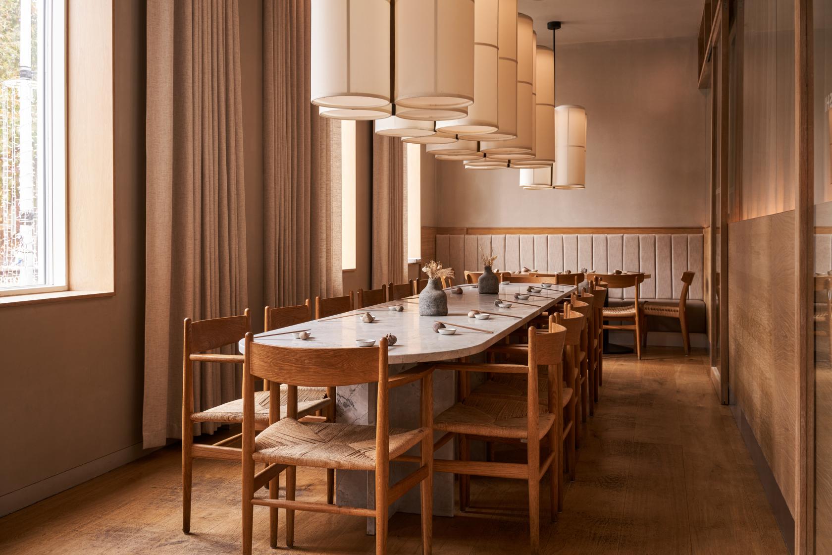 A dining room with a long marble-top table, wooden chairs, and pendant lights at Sticks'n'Sushi Chelsea.