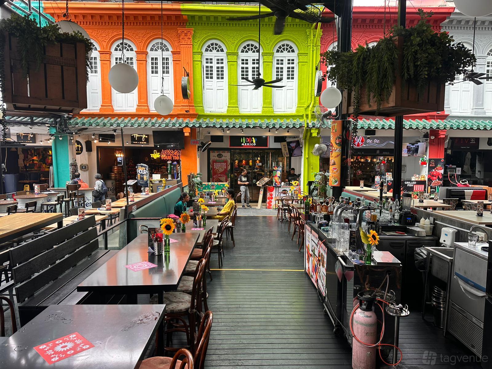 An outdoor restaurant space with wooden tables, sunflowers, and colorful facades at HOLA! MEXICO.