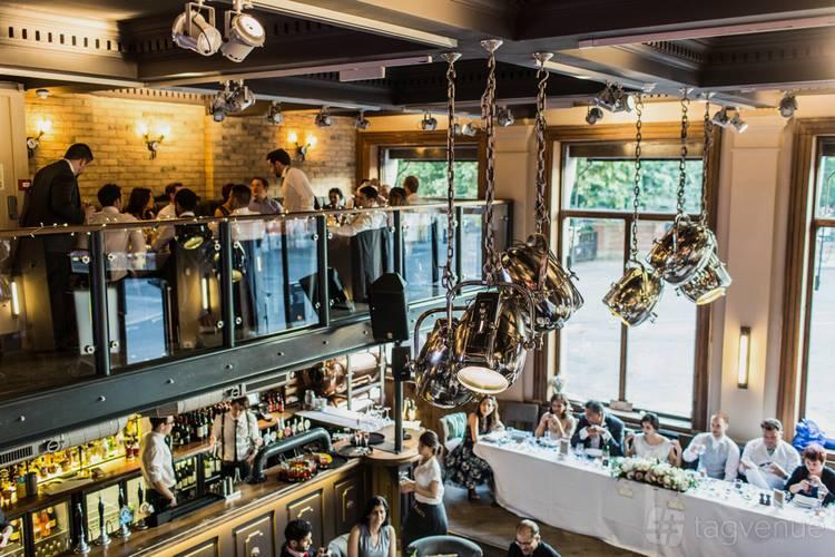 A restaurant with double-height ceilings, large windows, mezzanine seating, and a bar at Balfour St Bart's.