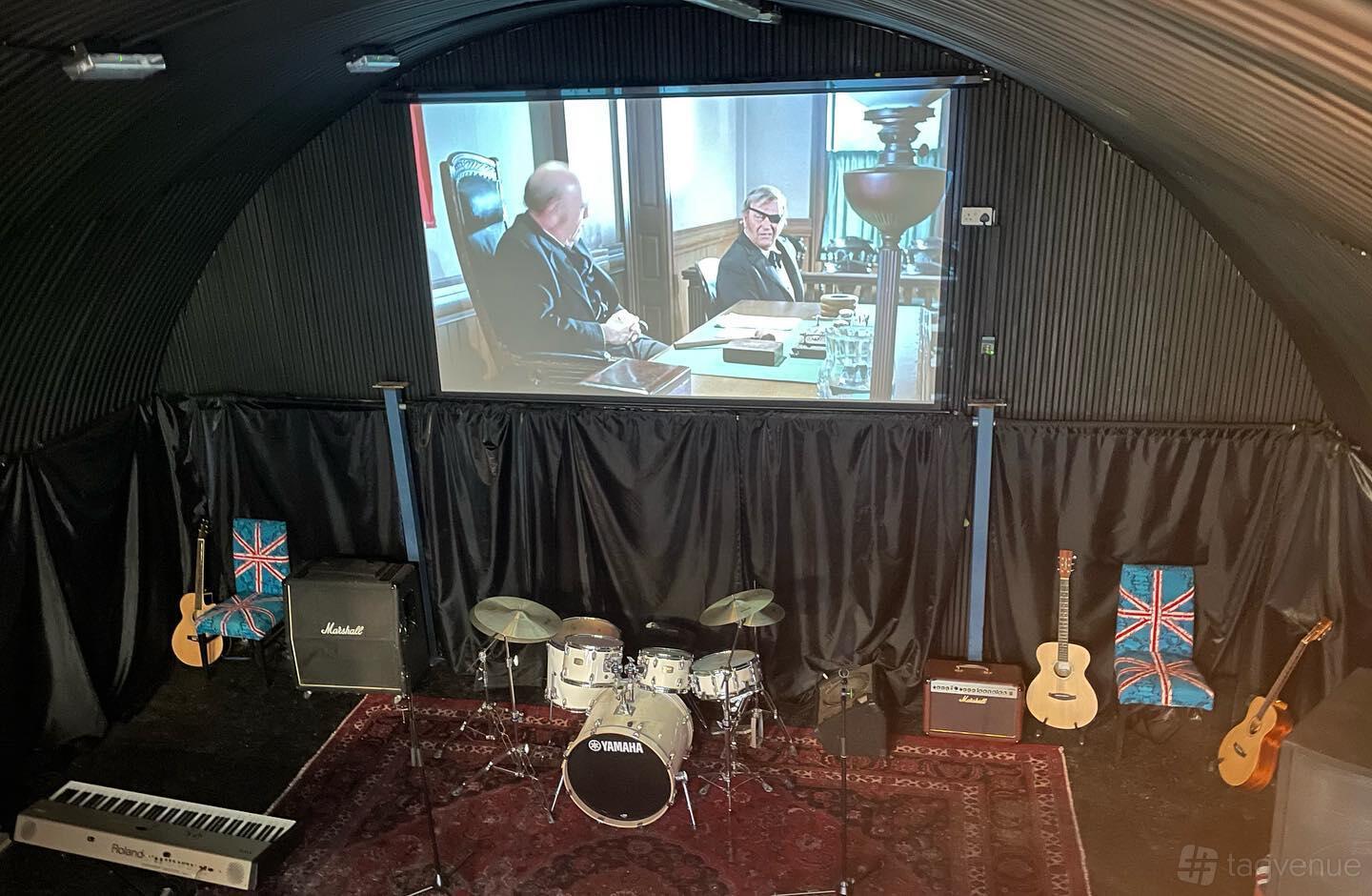A rehearsal studio with a drum kit, electric and acoustic guitars, amplifiers, and a large projector screen at The Secret London Pad.