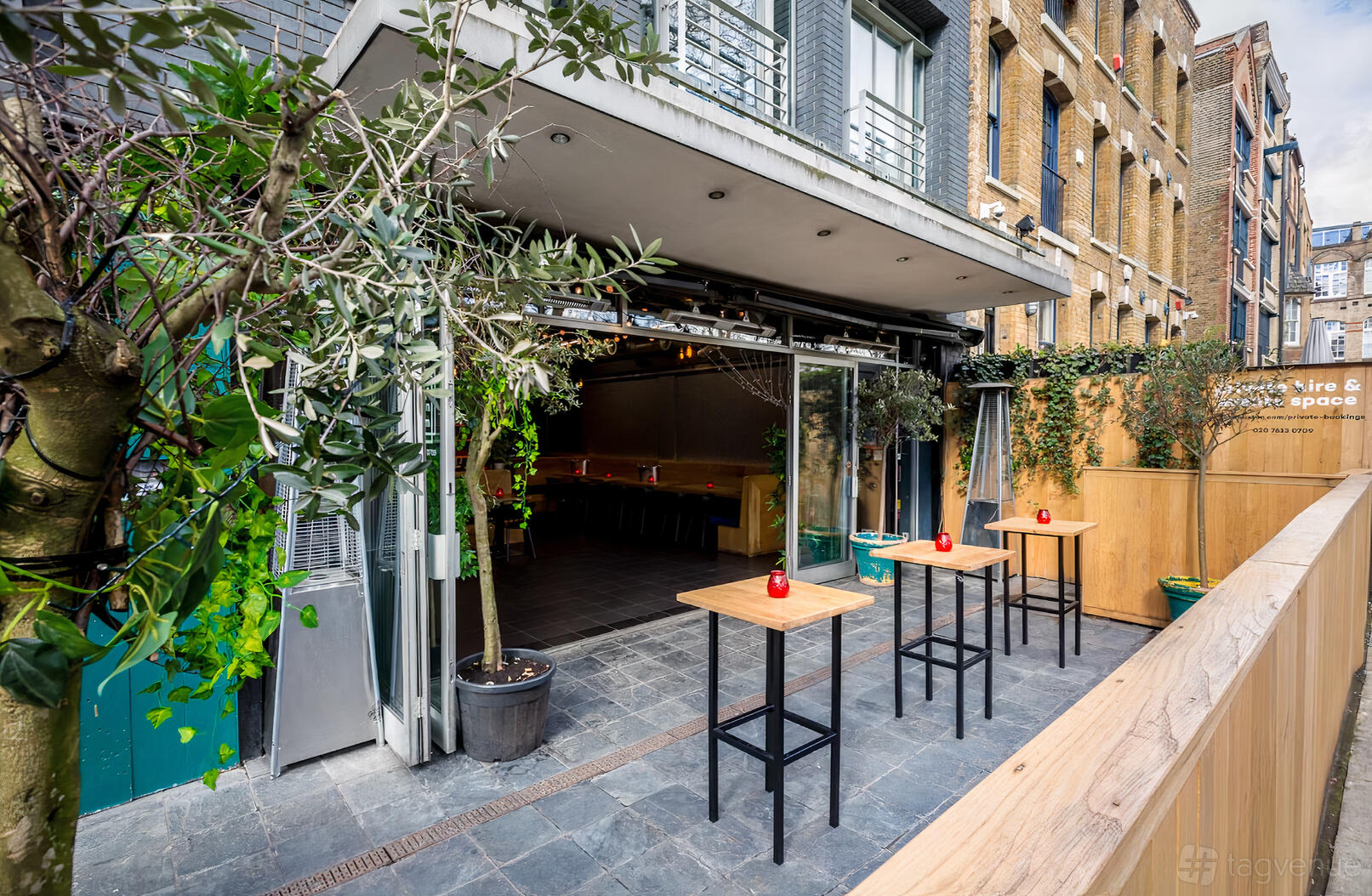 A versatile event space with floor-to-ceiling glass doors opening to a patio with tall tables at Colours Hoxton.