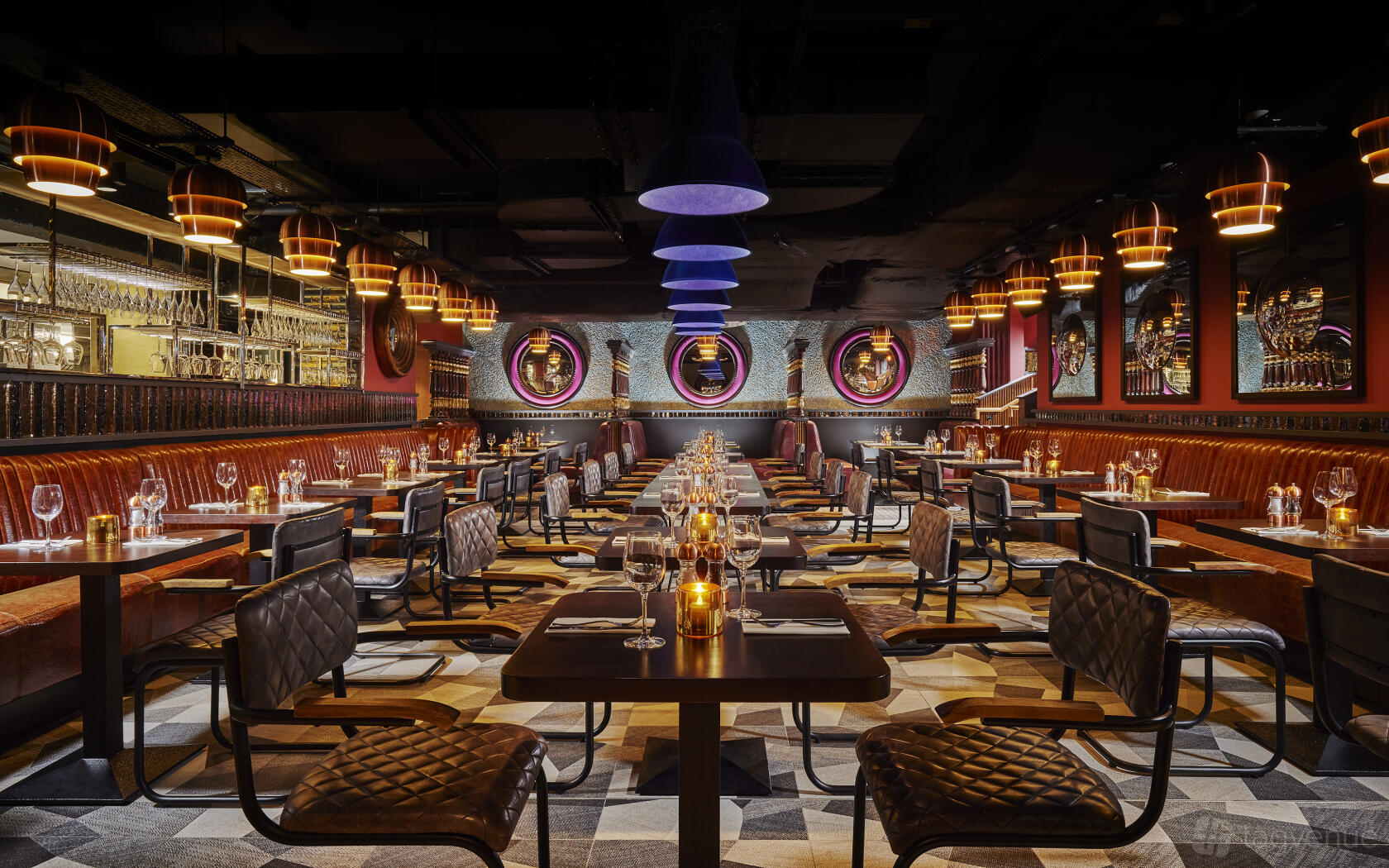 An event space in a restaurant with leather banquette seating, round mirrors, and candlelit tables at Bartley's Bar and Restaurant.